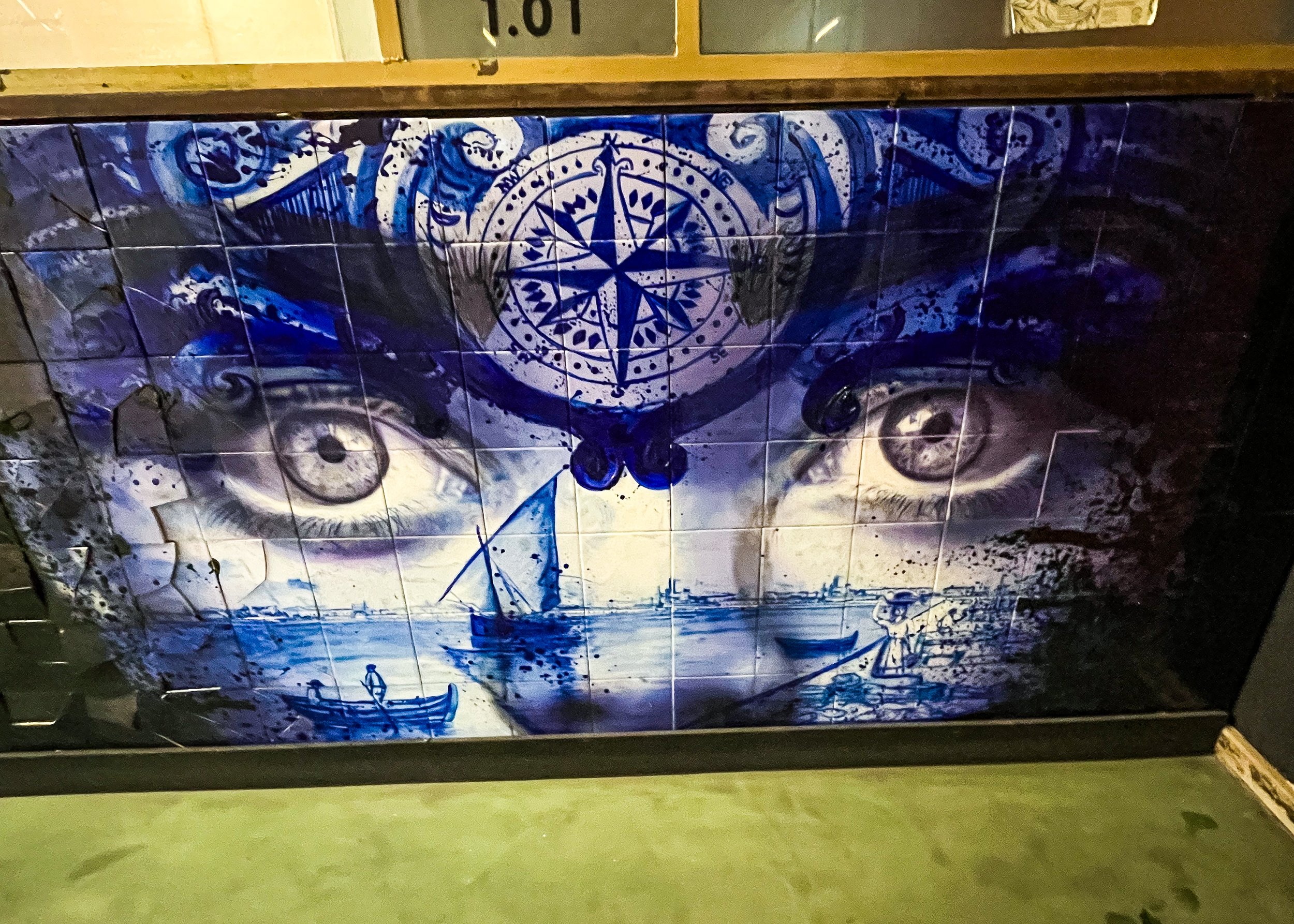 A tiled mural painted in blue, white, and black featuring a large compass rose, eye illustrations, and abstract decorative swirls, with a nautical theme.