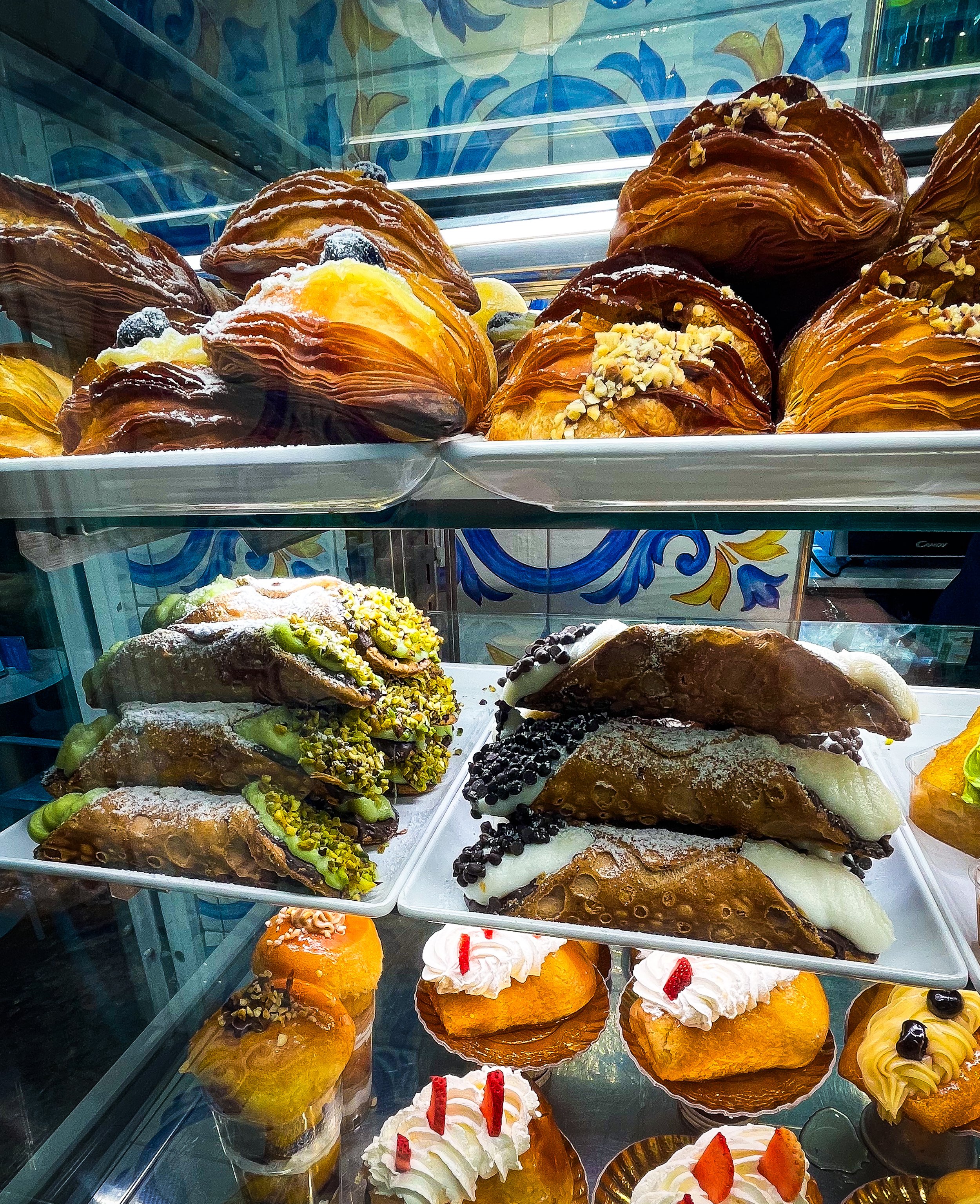 Display case filled with croissants and pastries topped with fruit, nuts, and whipped cream.