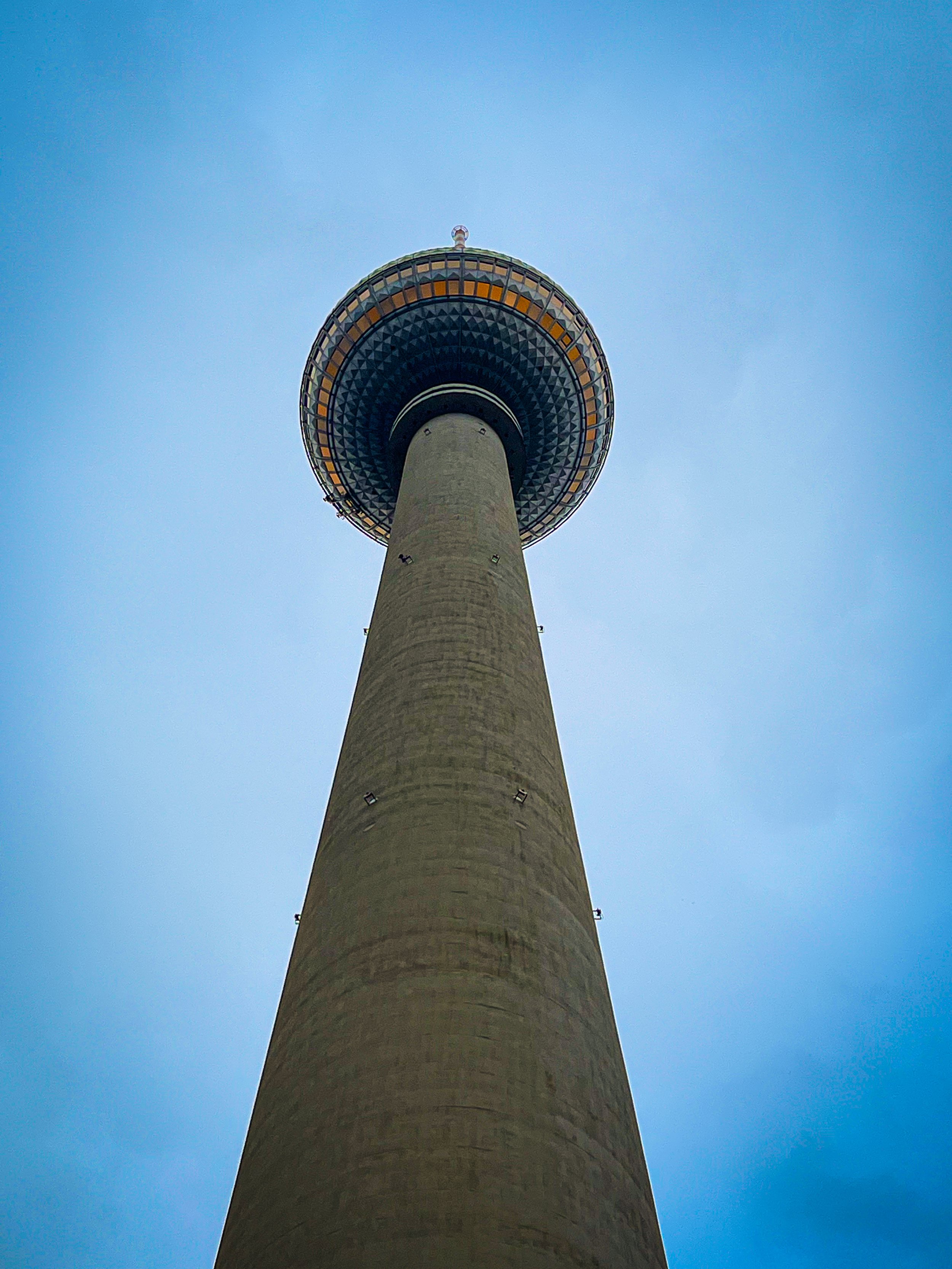 A tall observation tower viewed from below with a circular observation deck at the top, against a clear blue sky.