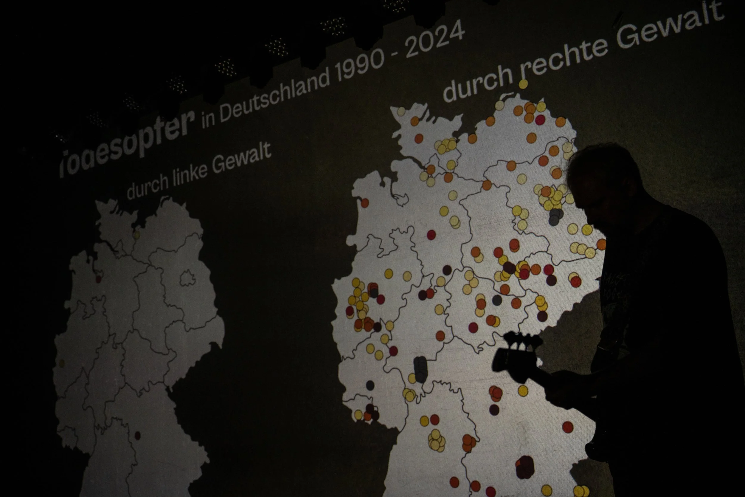 Schatten einer Person mit einem Elektrogitarren-ähnlichen Instrument vor einer Karte von Deutschland mit farbigen Punkten und Text zur Geschichte der Jagdsauper in Deutschland.