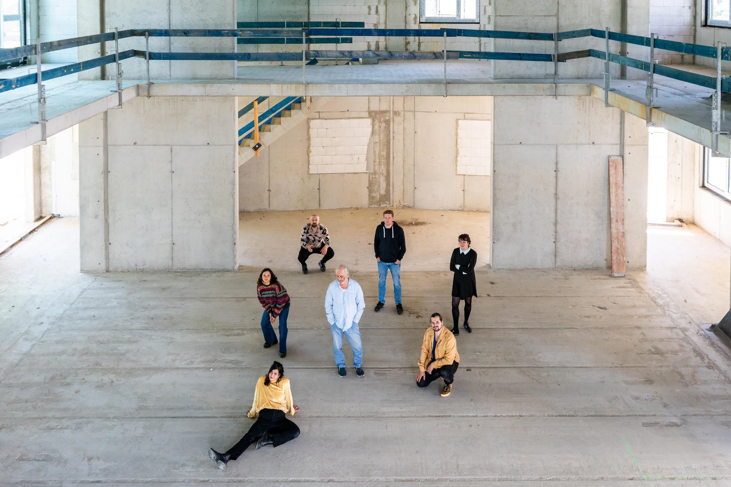 Das Team der Kammerspiele Magdeburg posiert in einem unvollendeten, rohen Gebäuderaum des neuen Theaters am Elbbahnhof.
