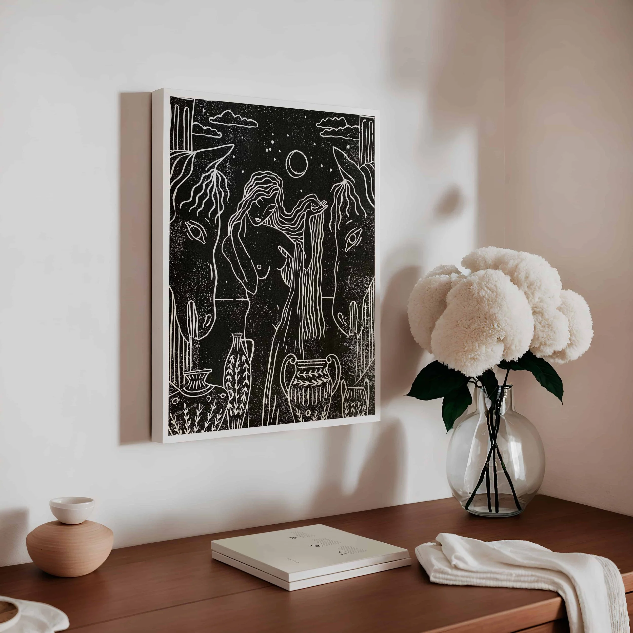 Der Linoldruck in Schwarz zeigt eine nackte Frau mit zwei Pferden. Das Linol wird von einem weißen Rahmen in einem modernen, beigefarbenen Interieur eingerahmt.
