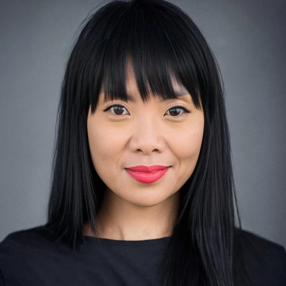 Close-up portrait of an Asian woman with straight black hair and bangs, smiling softly against a gray background.