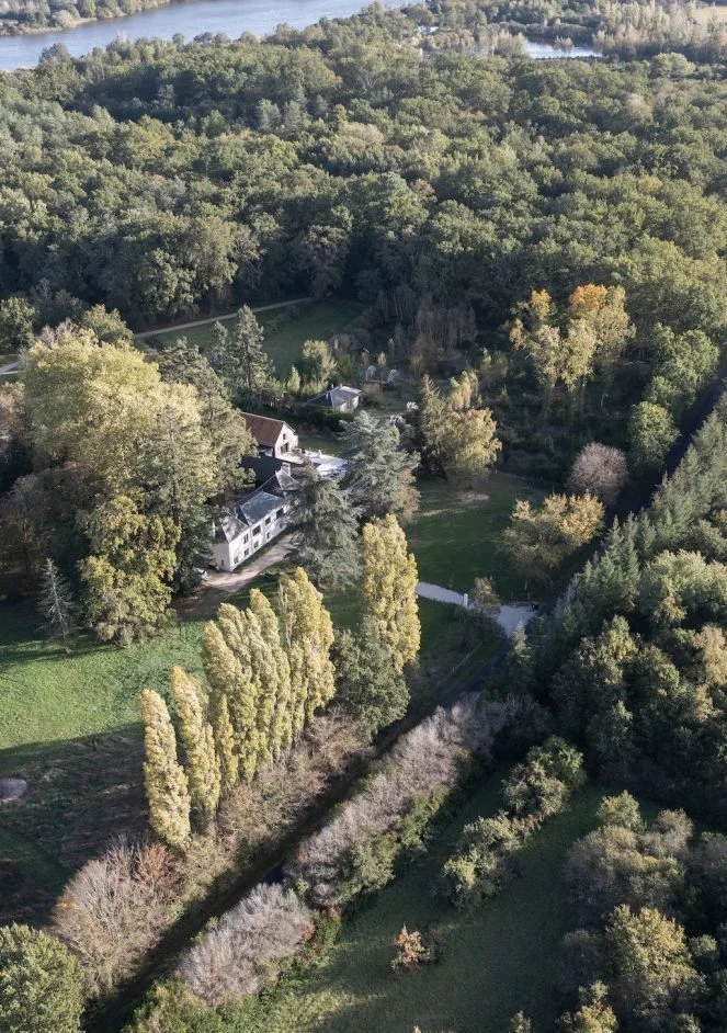 Aerial view of a large, historic estate surrounded by dense trees and landscaped gardens, with a river in the background.