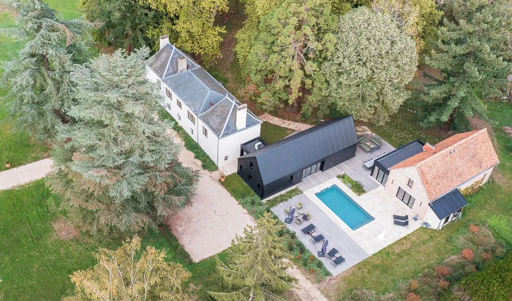 Aerial view of three connected houses surrounded by trees, with a swimming pool and outdoor seating area in the backyard.