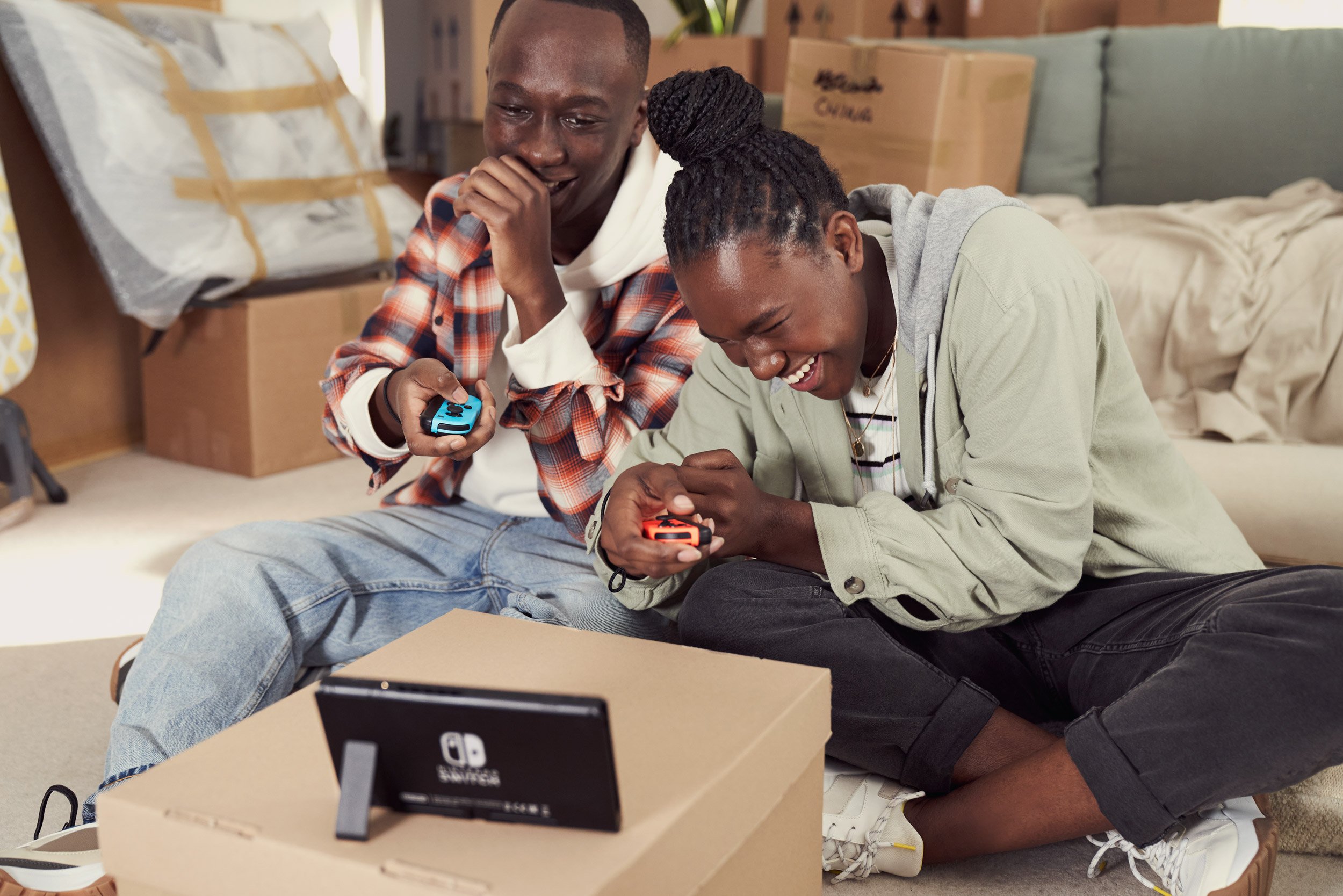 Two people sitting on the floor playing a video game, a Nintendo Switch, with a blue and red controller.