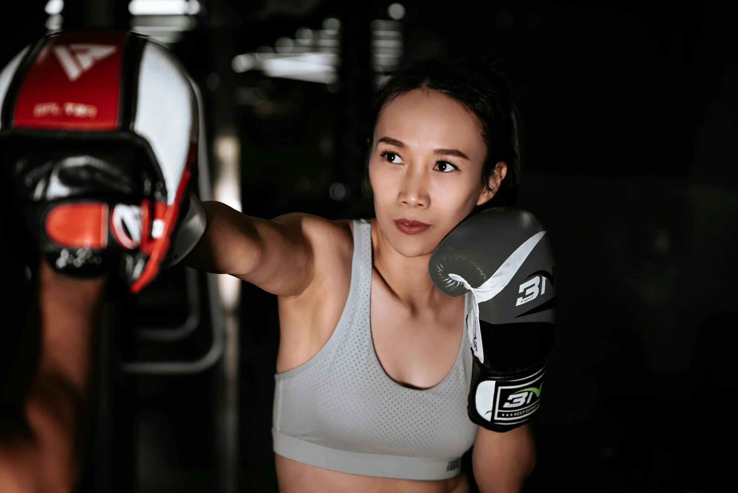 A young woman with dark hair training with boxing gloves in a gym.