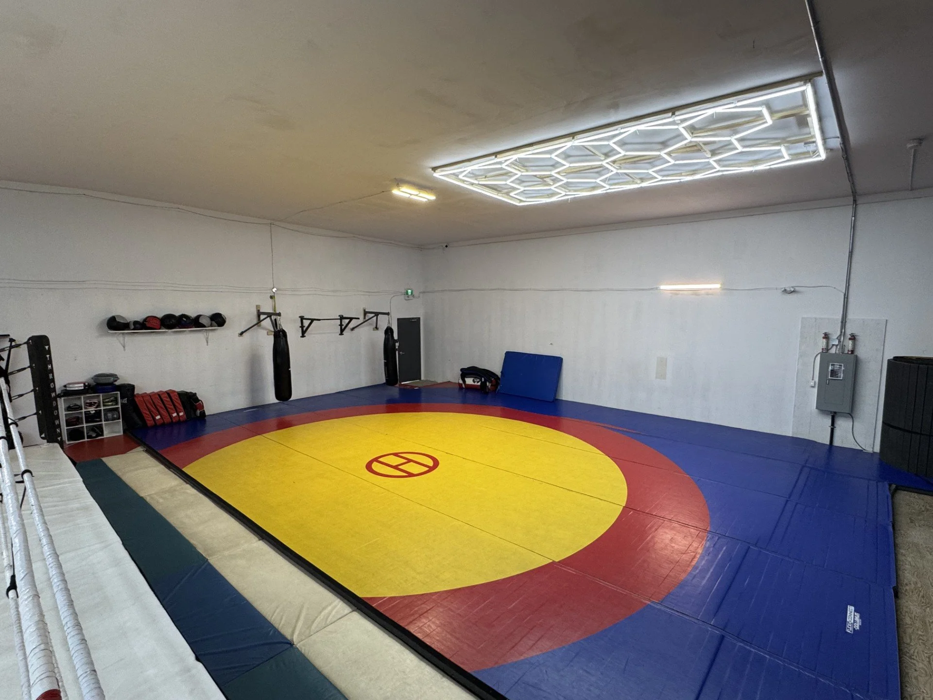 Interior of a modern gym with various equipment including boxing bags, weightlifting racks, and benches, with motivational banners on the walls.