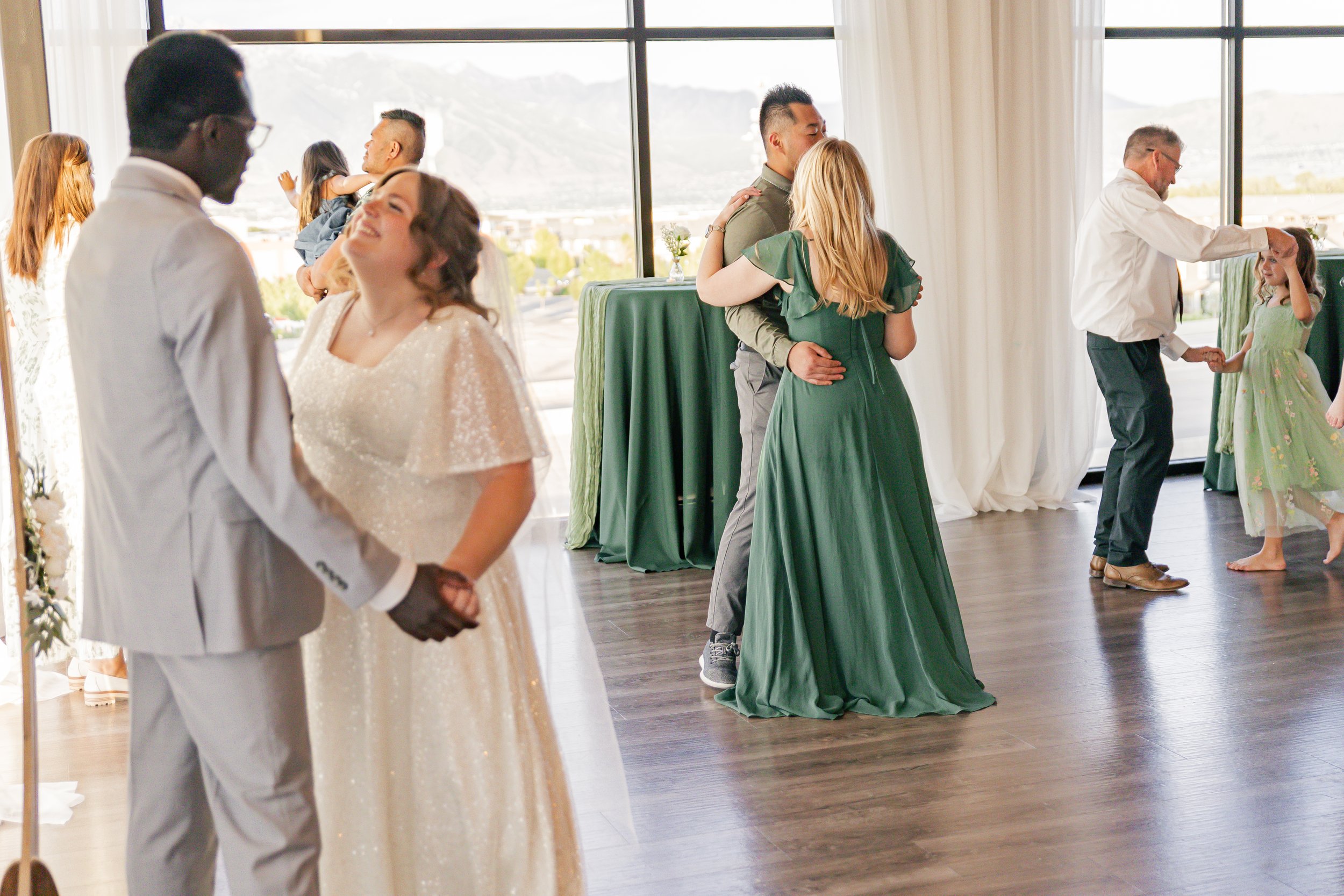 Couples dancing at a wedding reception in a bright, scenic venue with large windows and mountain views.