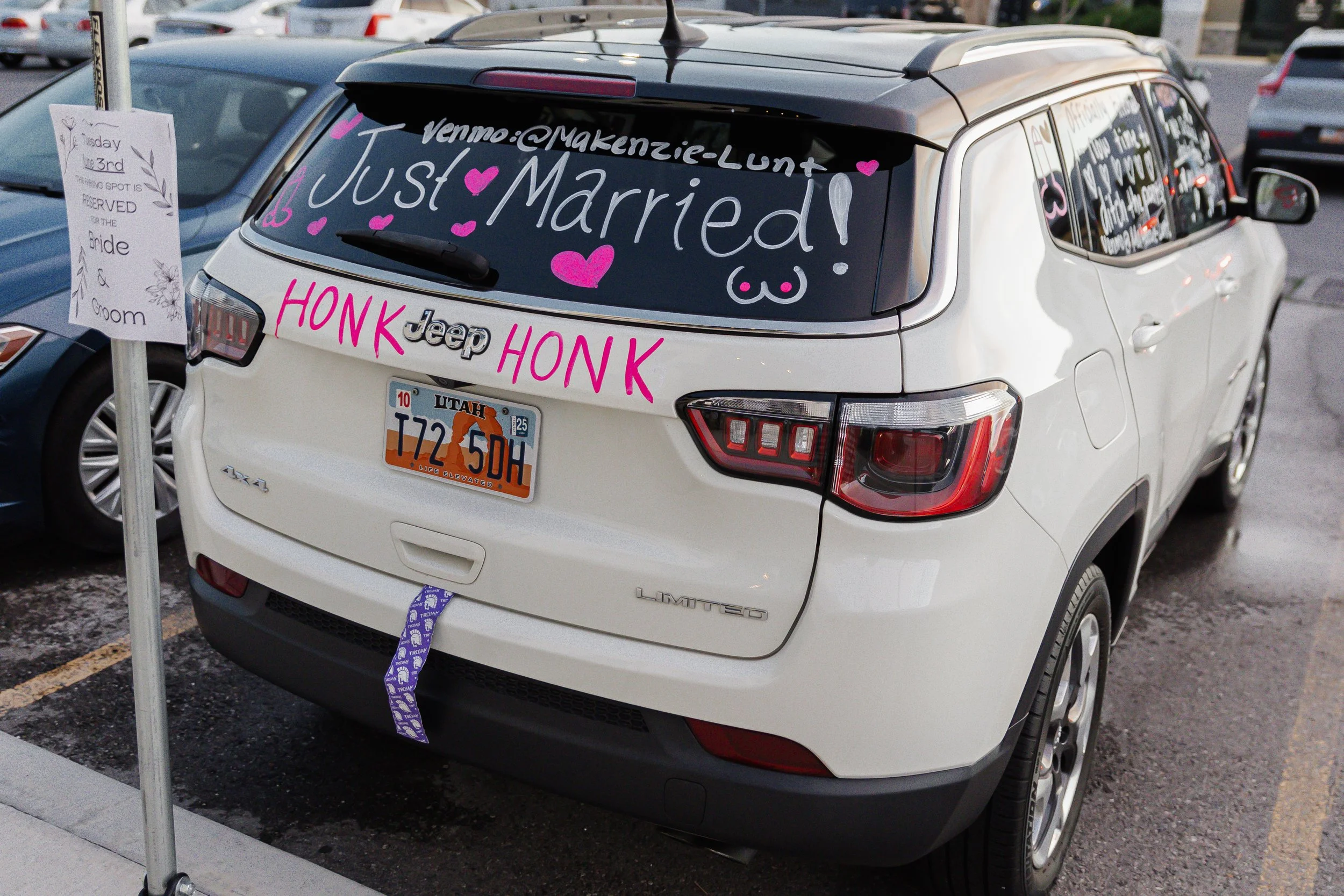 White Jeep SUV parked in a lot with wedding decorations and messages on the rear window indicating a marriage celebration.