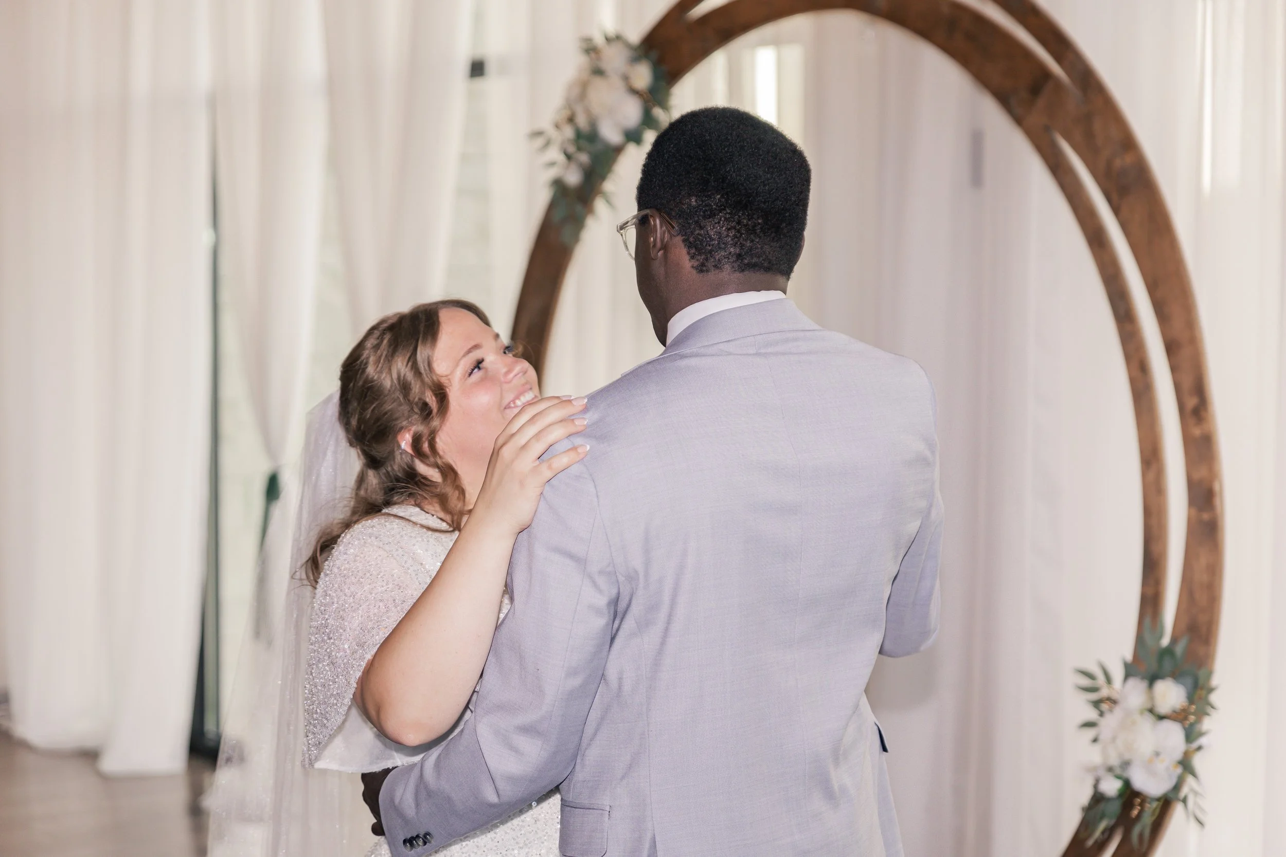 Bride and groom sharing a moment under a wooden arch at their wedding ceremony.