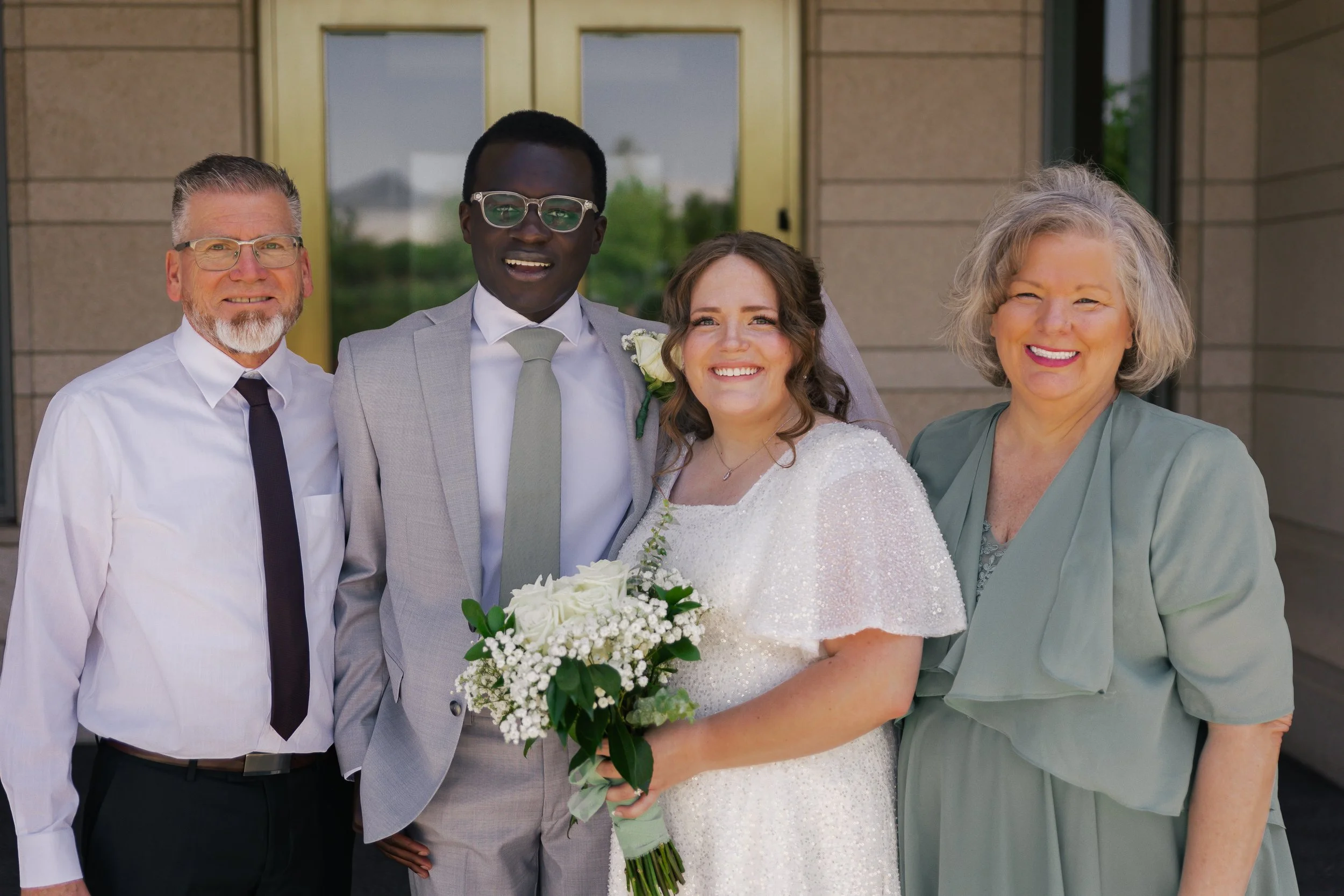 A smiling bride and groom standing with two older women outside a building.