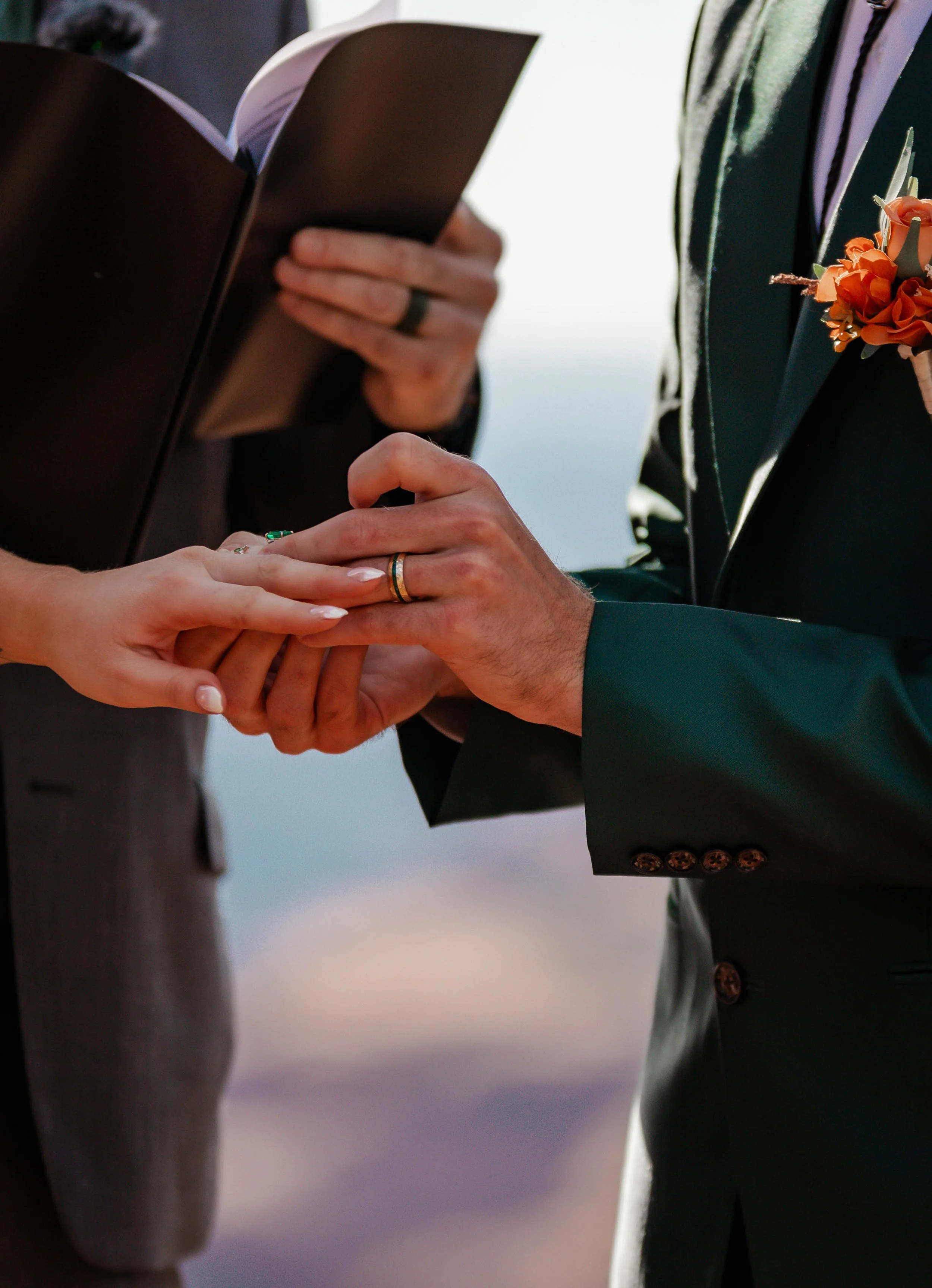 A couple getting married, exchanging rings during their wedding ceremony outdoors.