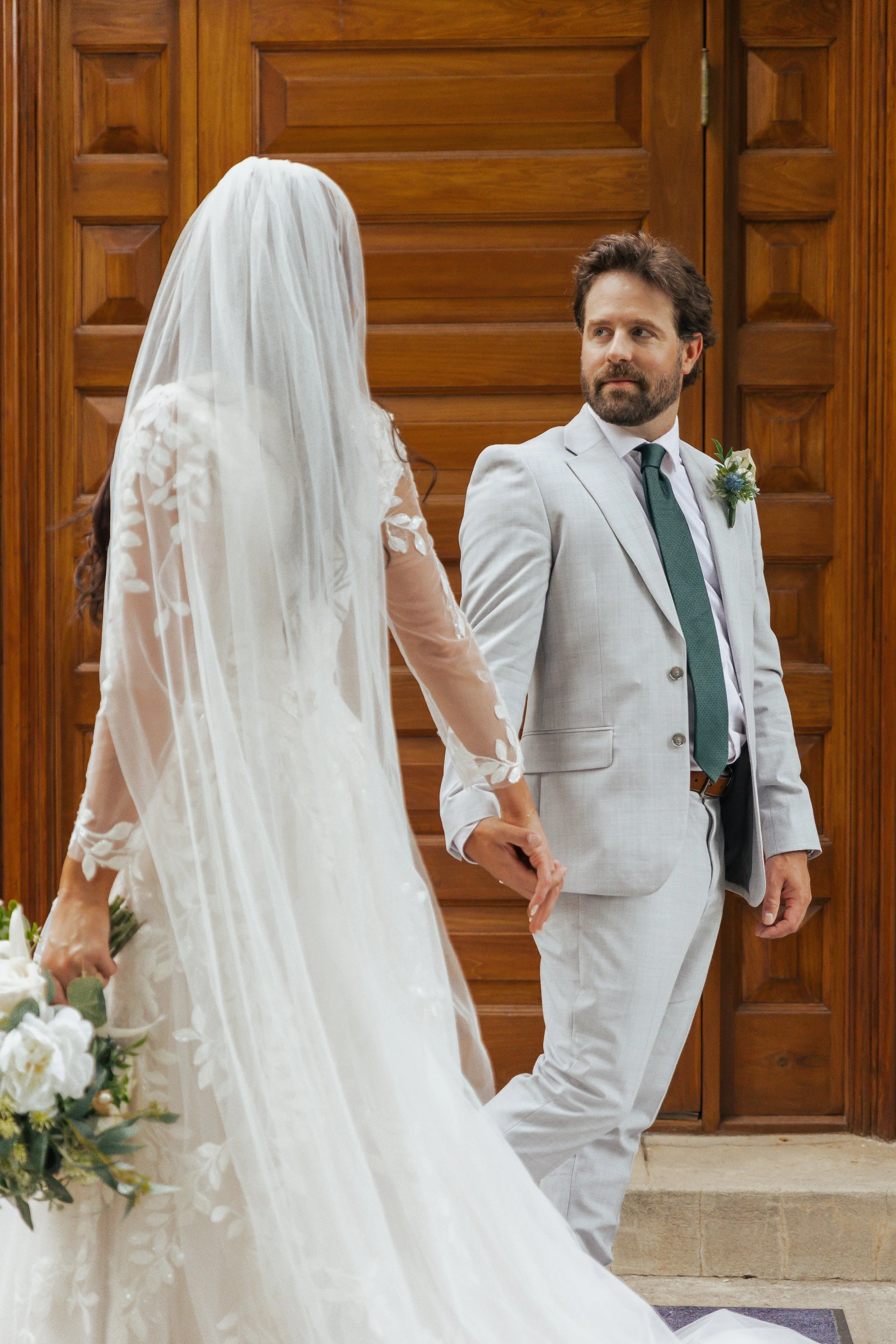 A bride and groom holding hands during their wedding ceremony inside a wooden-paneled room.