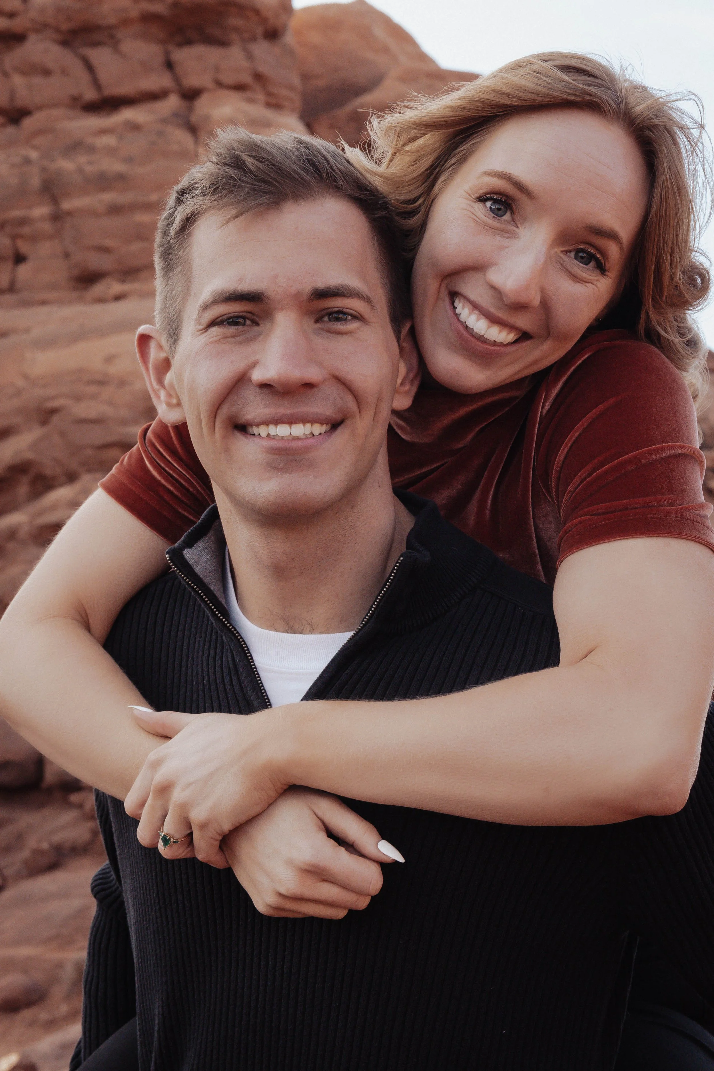 A smiling man and woman enjoying a moment outdoors with red rock formations in the background.