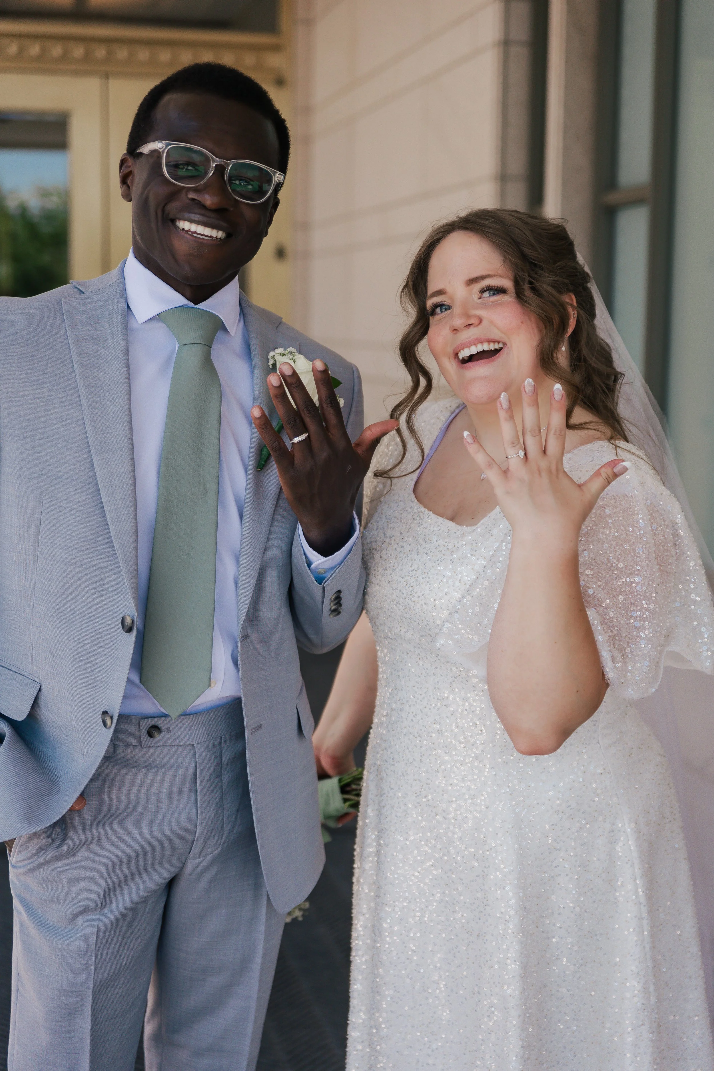 A newlywed couple showing off their wedding rings and smiling.