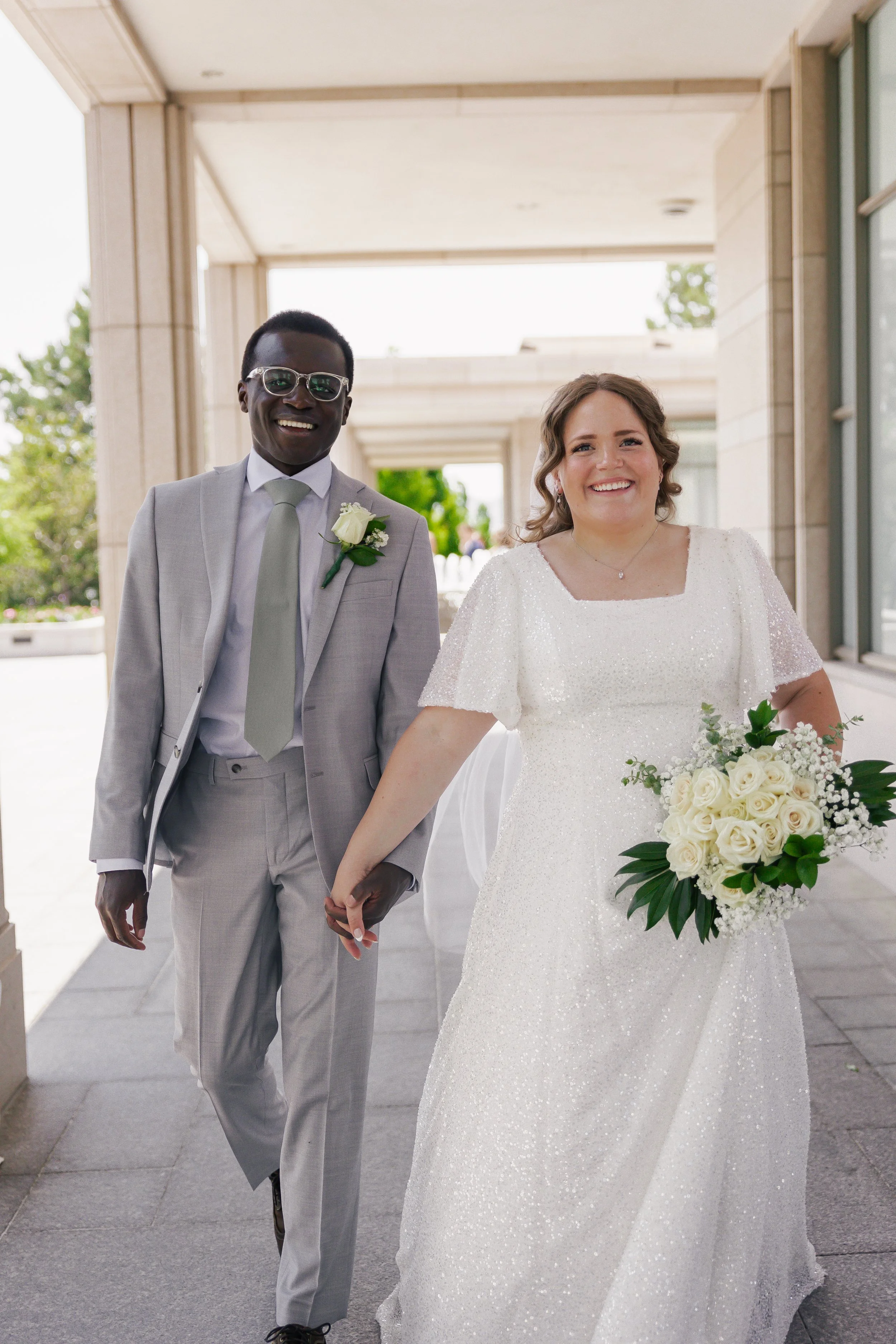 A smiling bride and groom holding hands and walking outside on their wedding day.