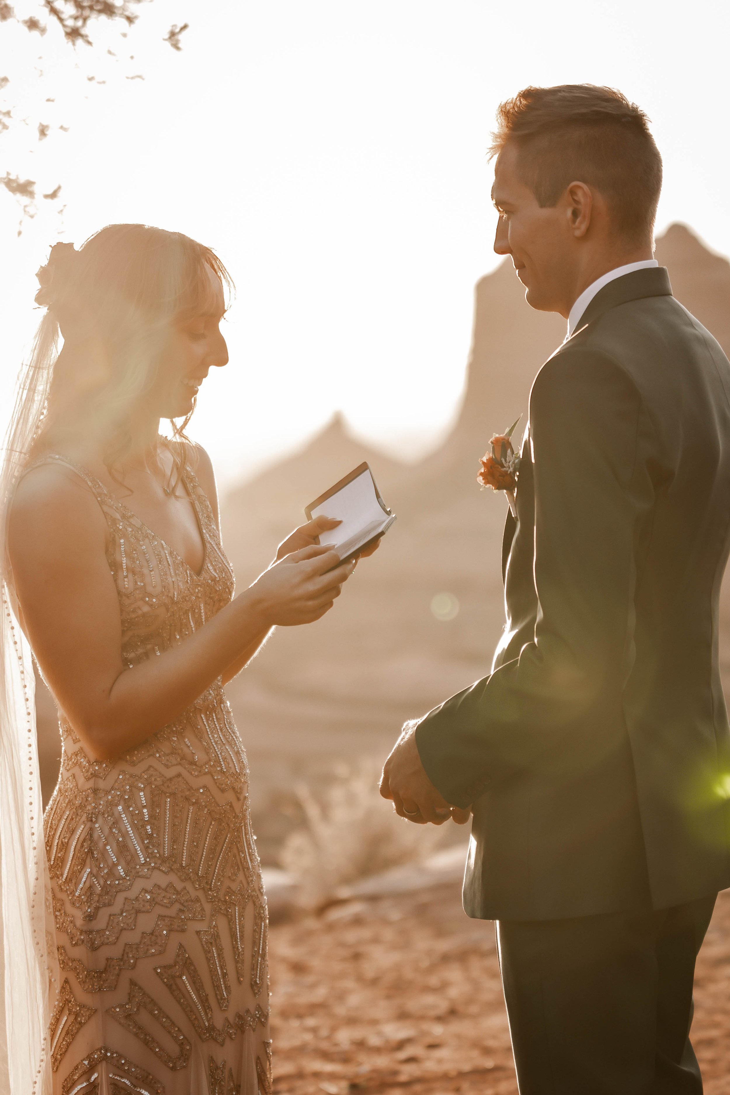 A bride and groom exchange vows during their outdoor wedding at sunset, in a desert landscape.