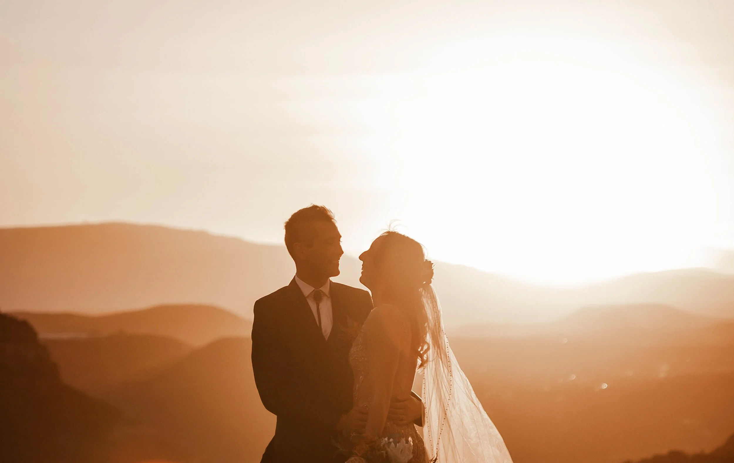 Silhouettes of a bride and groom standing close together at sunset in a desert landscape.