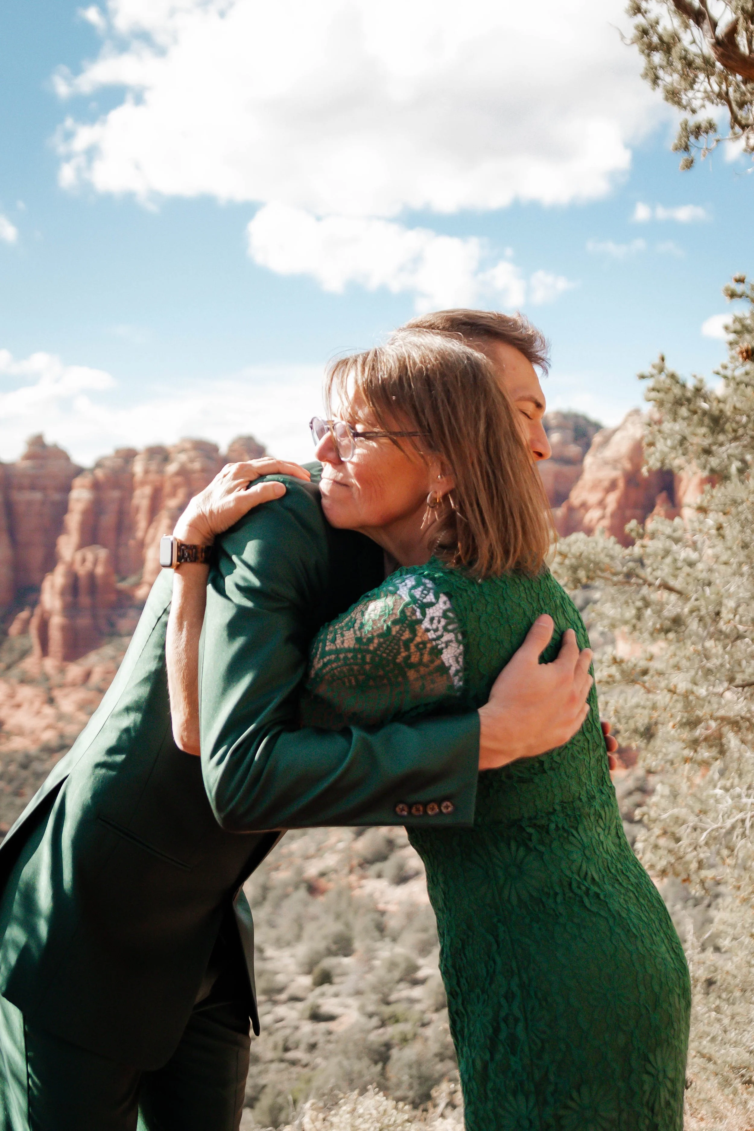 Two people embracing outdoors with red rock formations and a blue sky in the background.