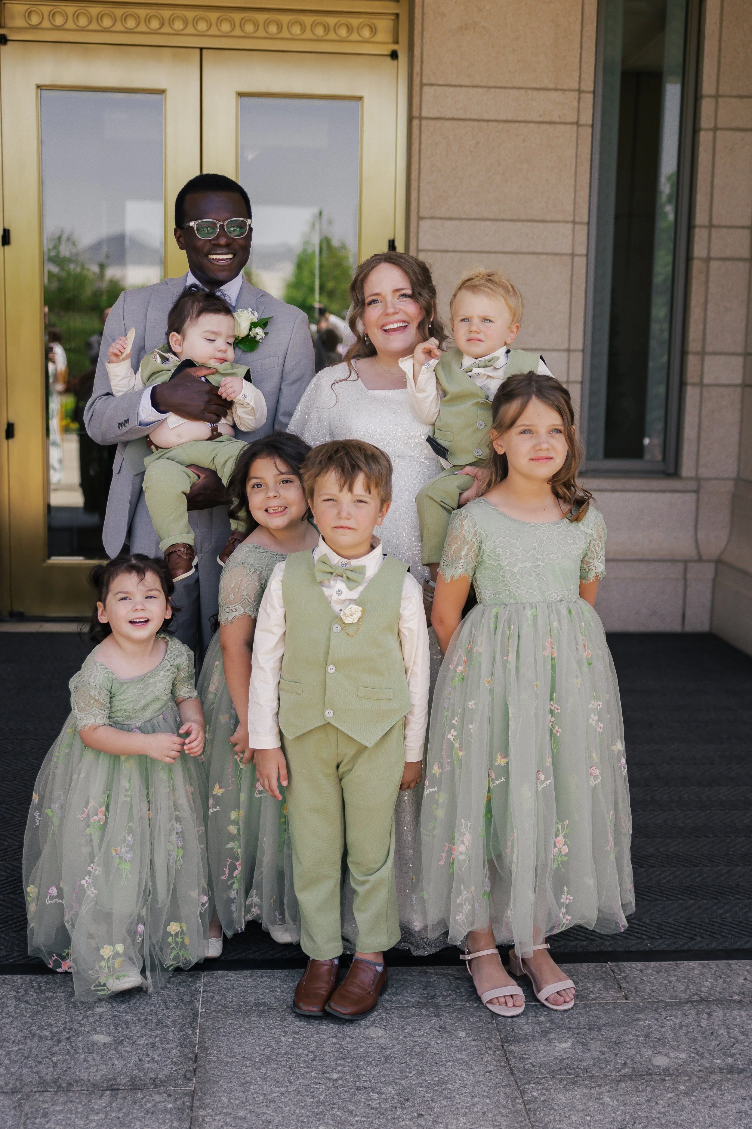 A group of people standing in front of a building with a golden door, smiling and dressed in formal attire, likely at a wedding or special event.