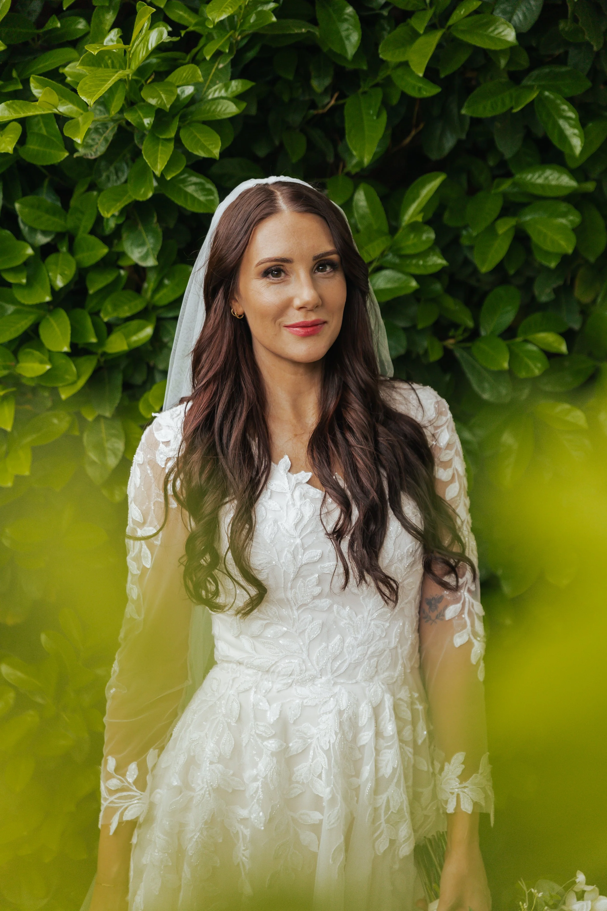 A woman in a wedding dress standing in front of green leafy bushes.