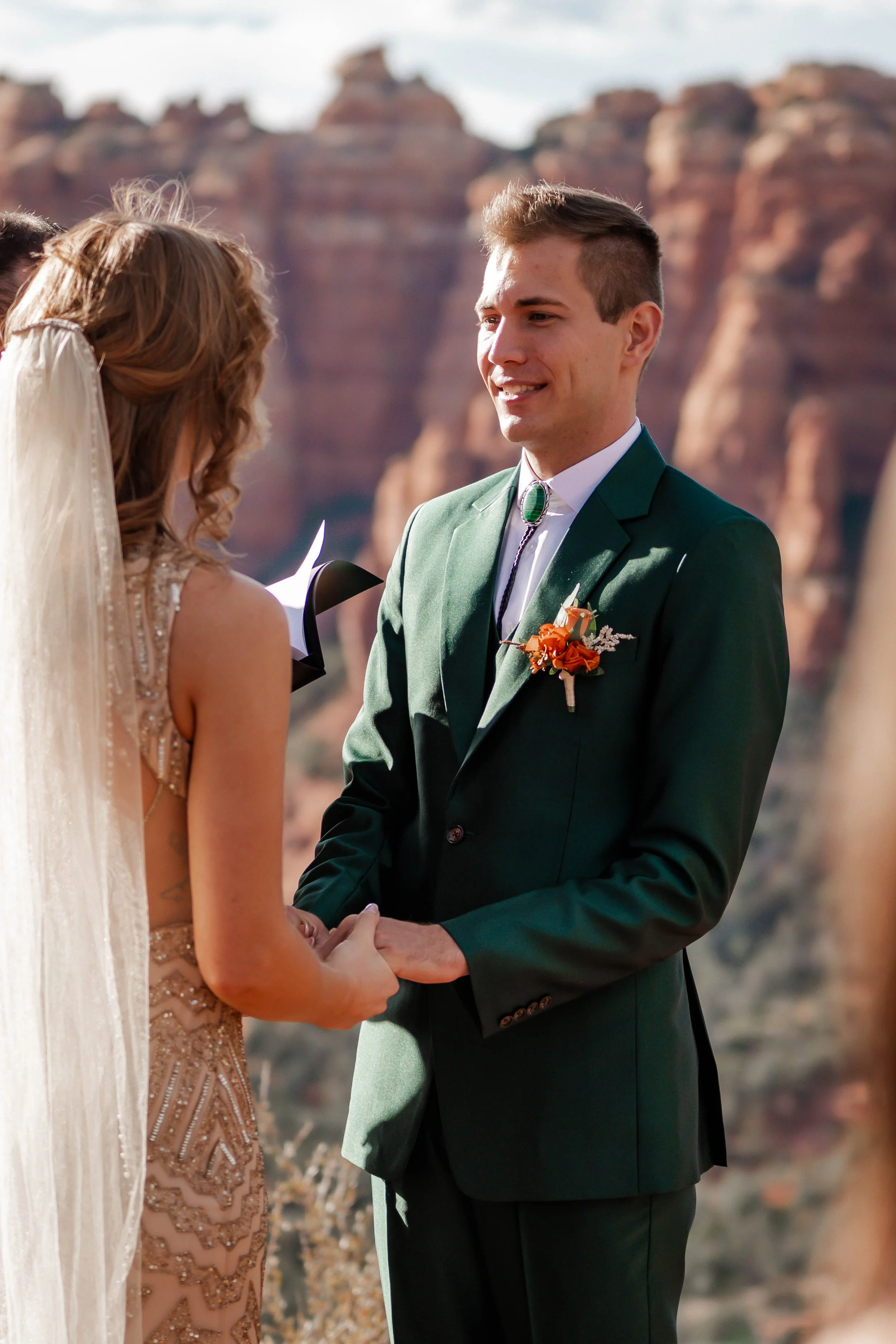 A couple exchanging wedding vows outdoors with red rock formations in the background.