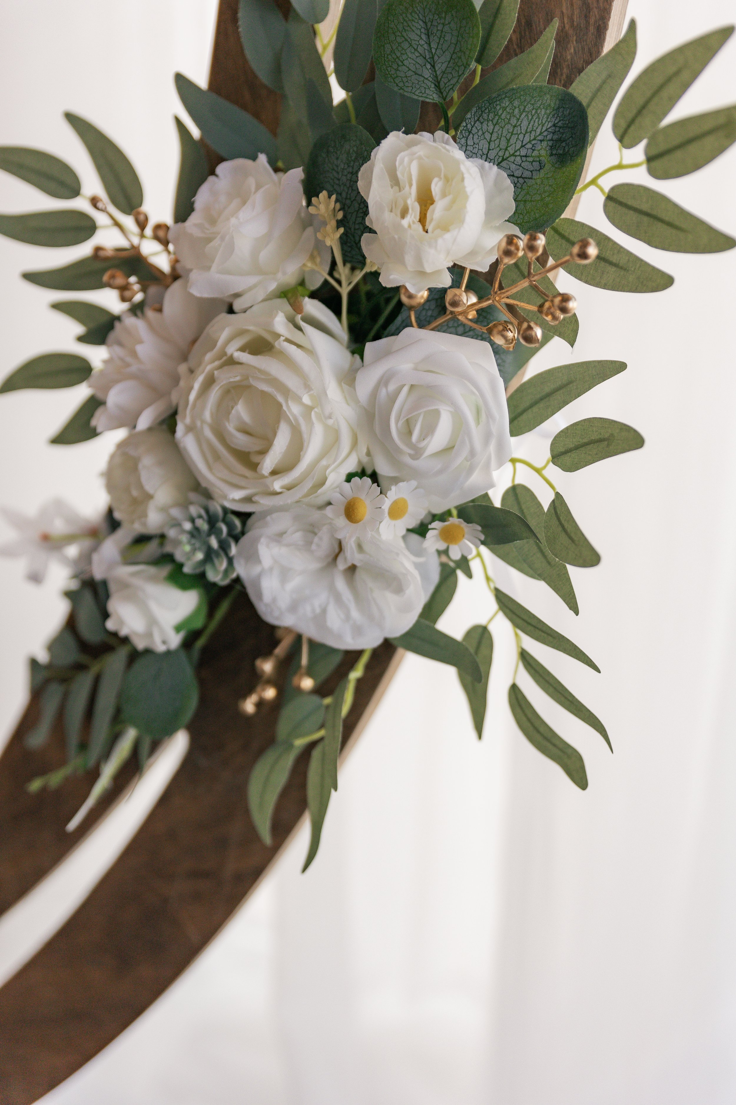 Close-up of an artificial flower arrangement with white roses, daisies, and green foliage attached to a wooden surface.