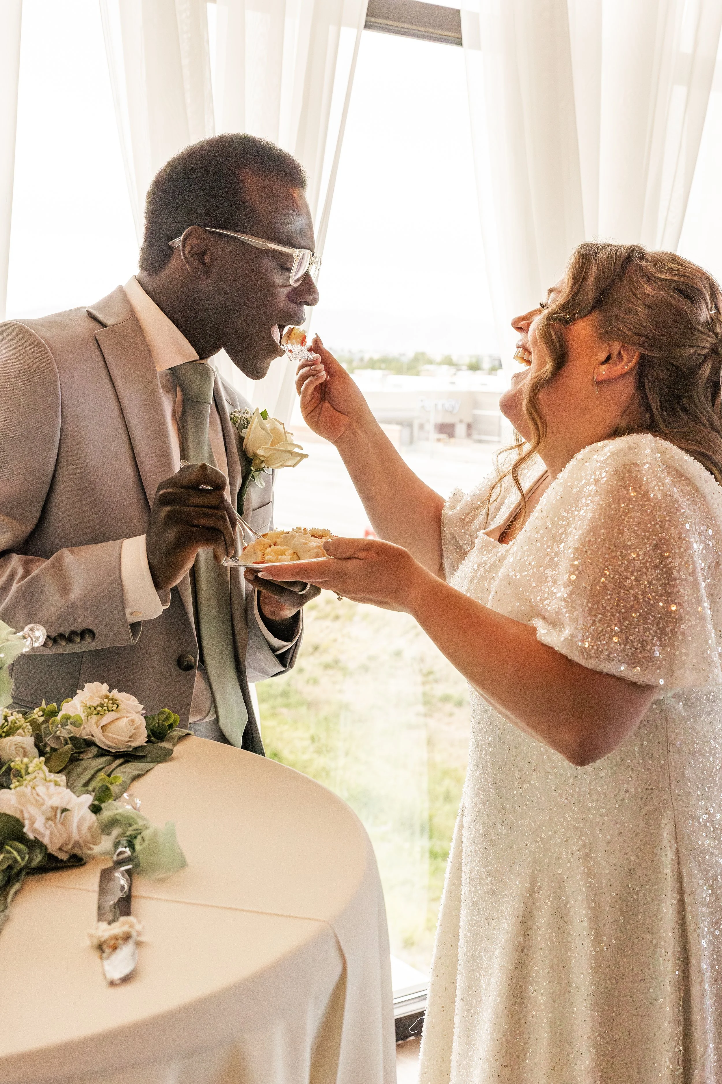 A bride and groom sharing their wedding cake during their reception, with the bride feeding cake to the groom.