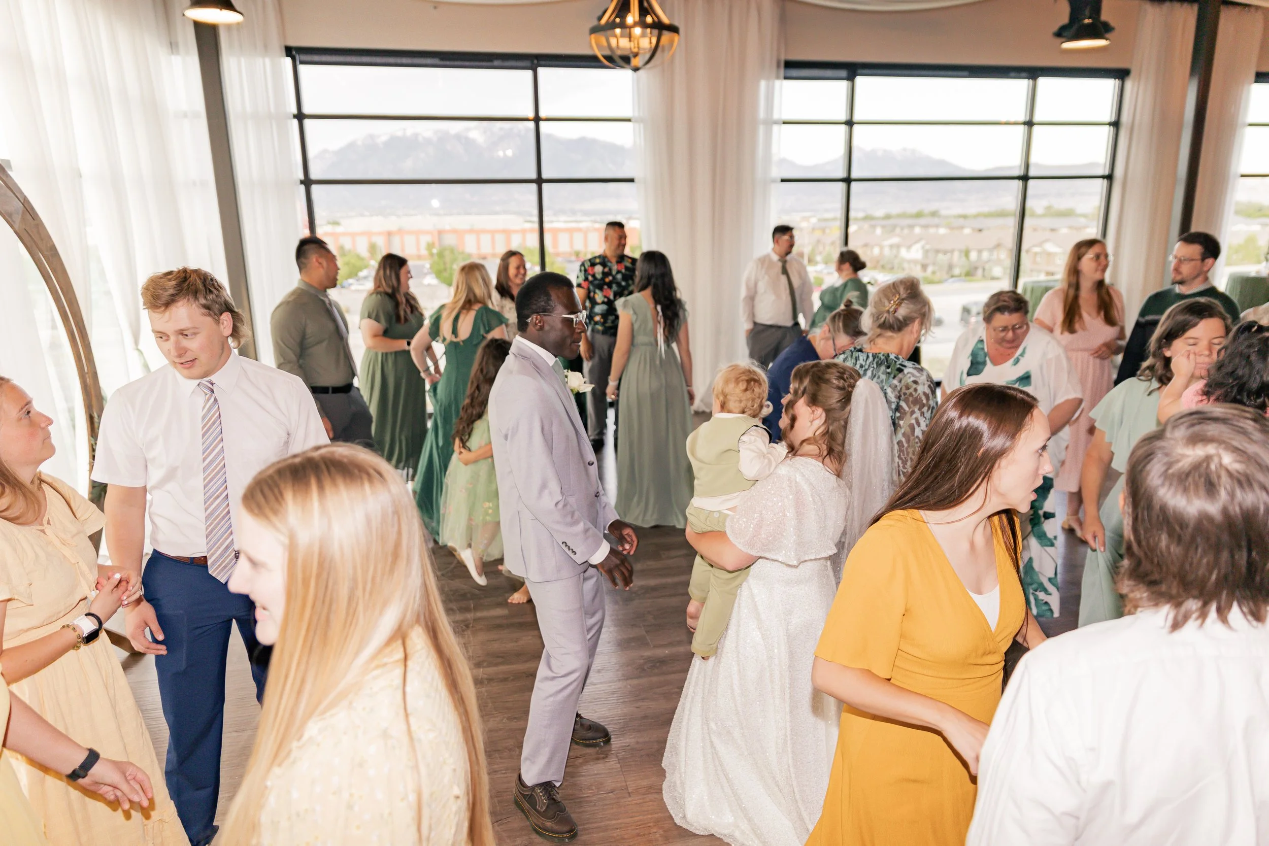 People dancing and socializing at an indoor event with large windows showing mountains in the background.