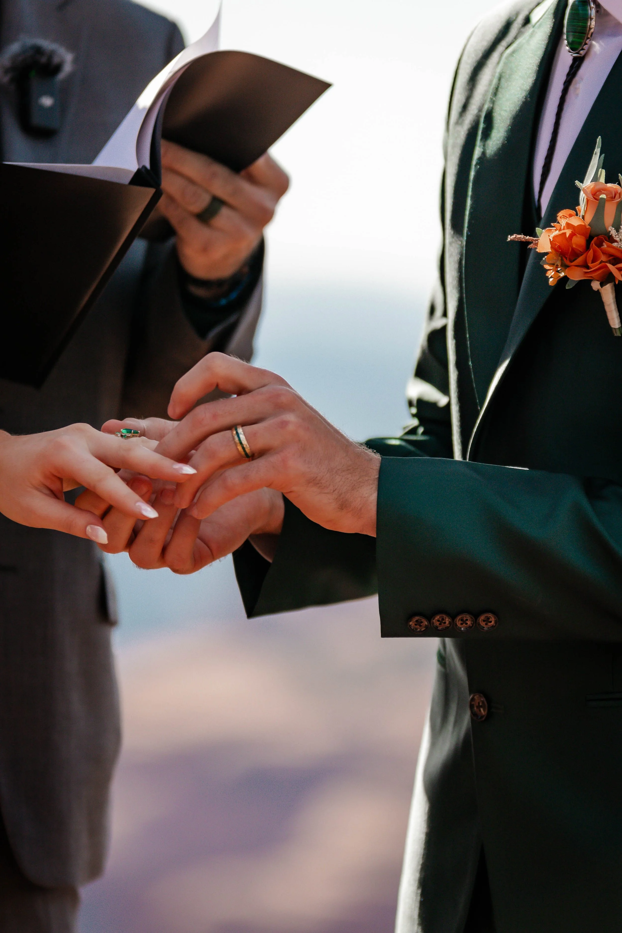 Close-up of a couple exchanging wedding rings during a wedding ceremony, with the bride placing a ring on the groom's finger.
