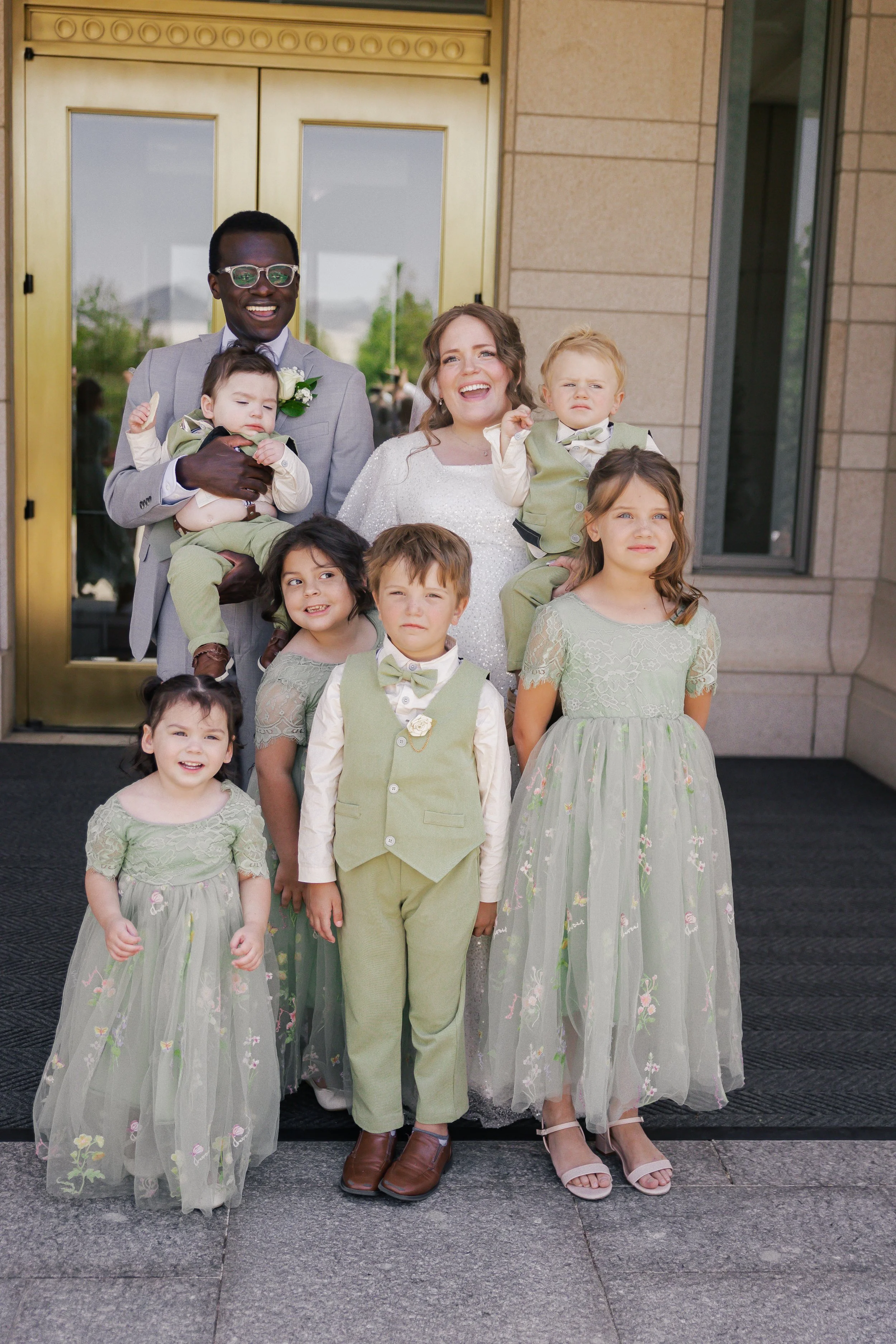 A group of nine people, including a bride, groom, and children, standing outside a building with a gold door, posing for a wedding photo.