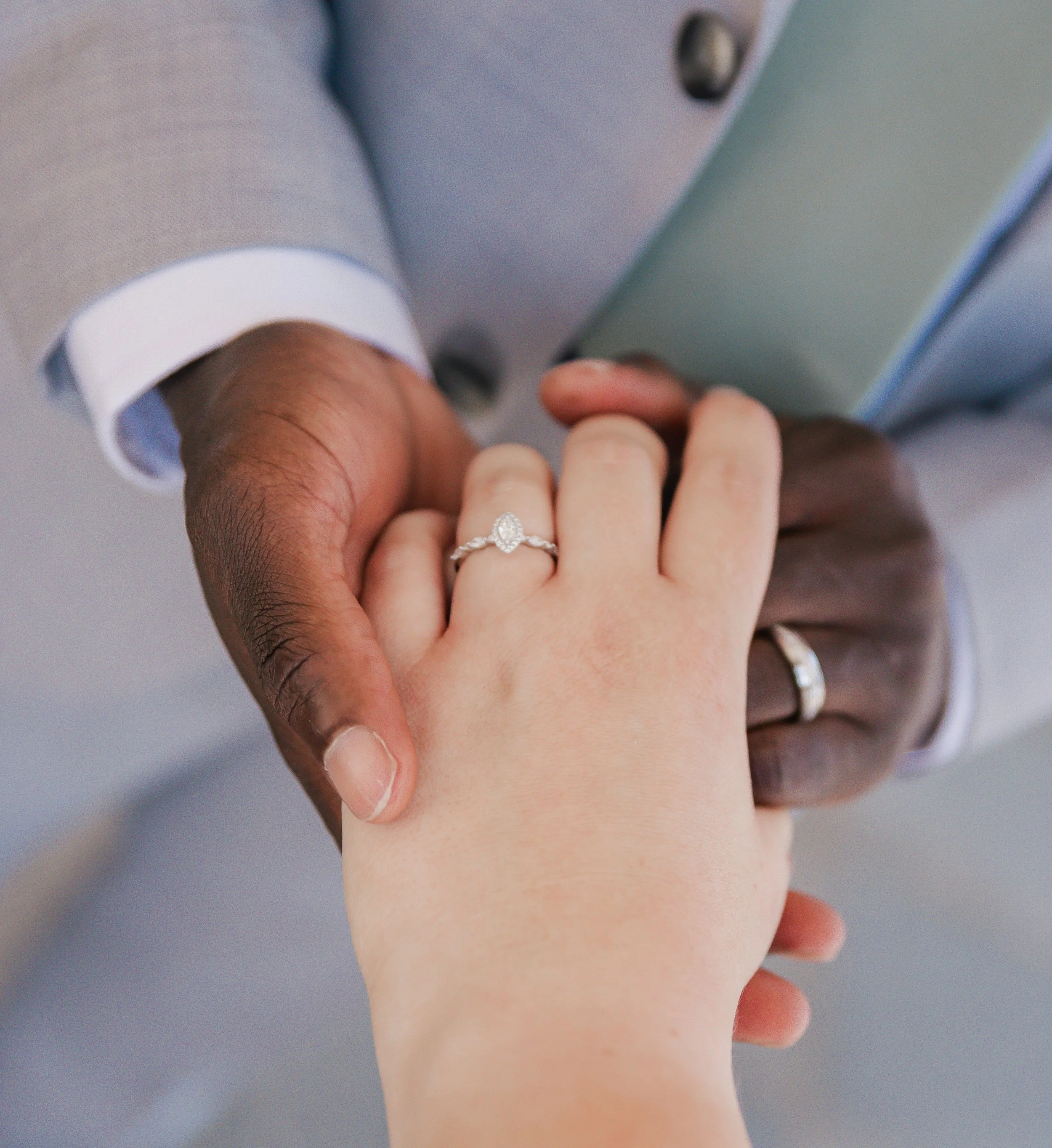 A couple holding hands, showing their wedding rings. The woman's hand is on top, with a diamond ring, and the man's hand is underneath.