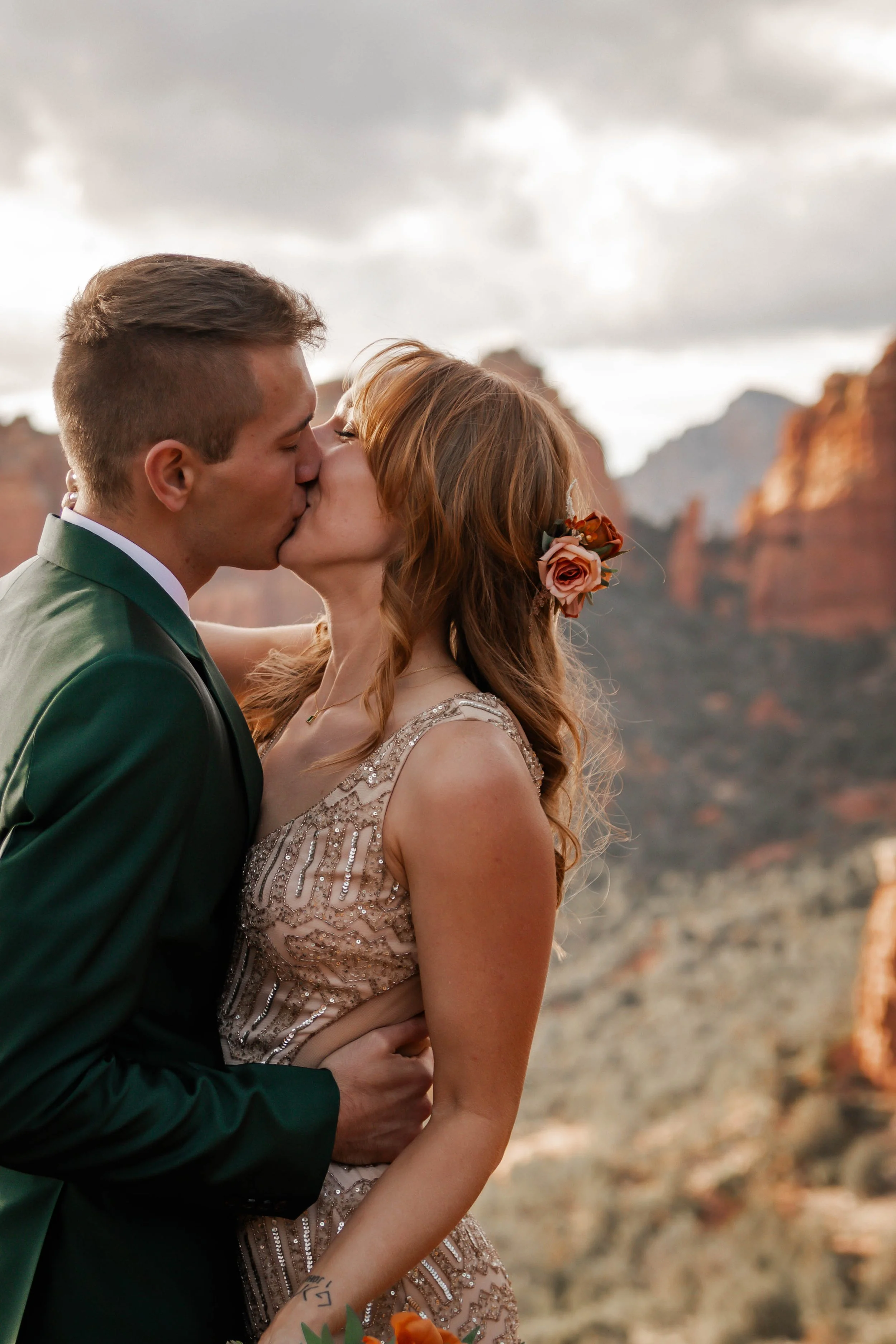 A couple kissing outdoors with rock formations in the background during daylight.
