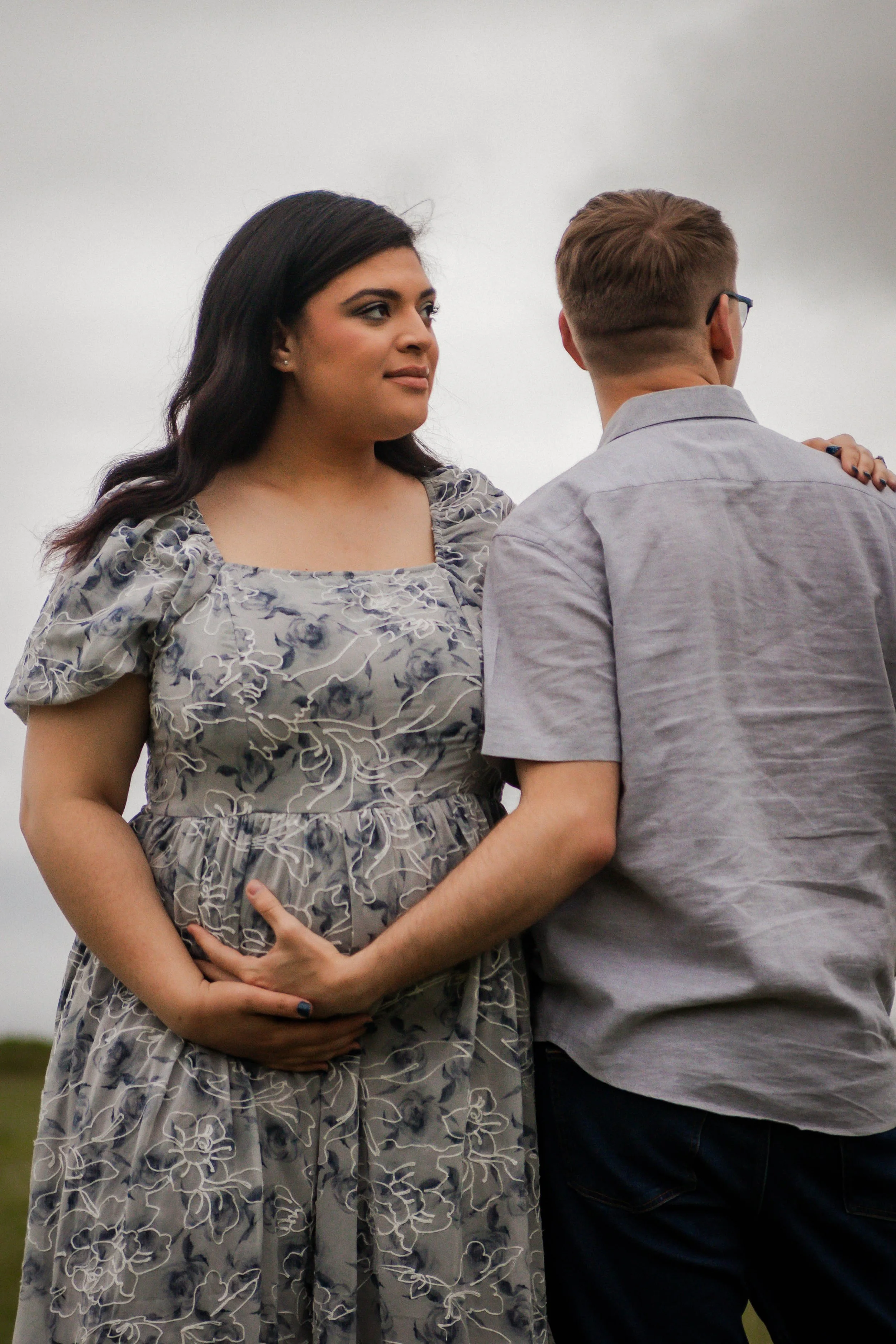 Photo of a pregnant woman wearing a grey dress standing next to a man wearing a grey shirt