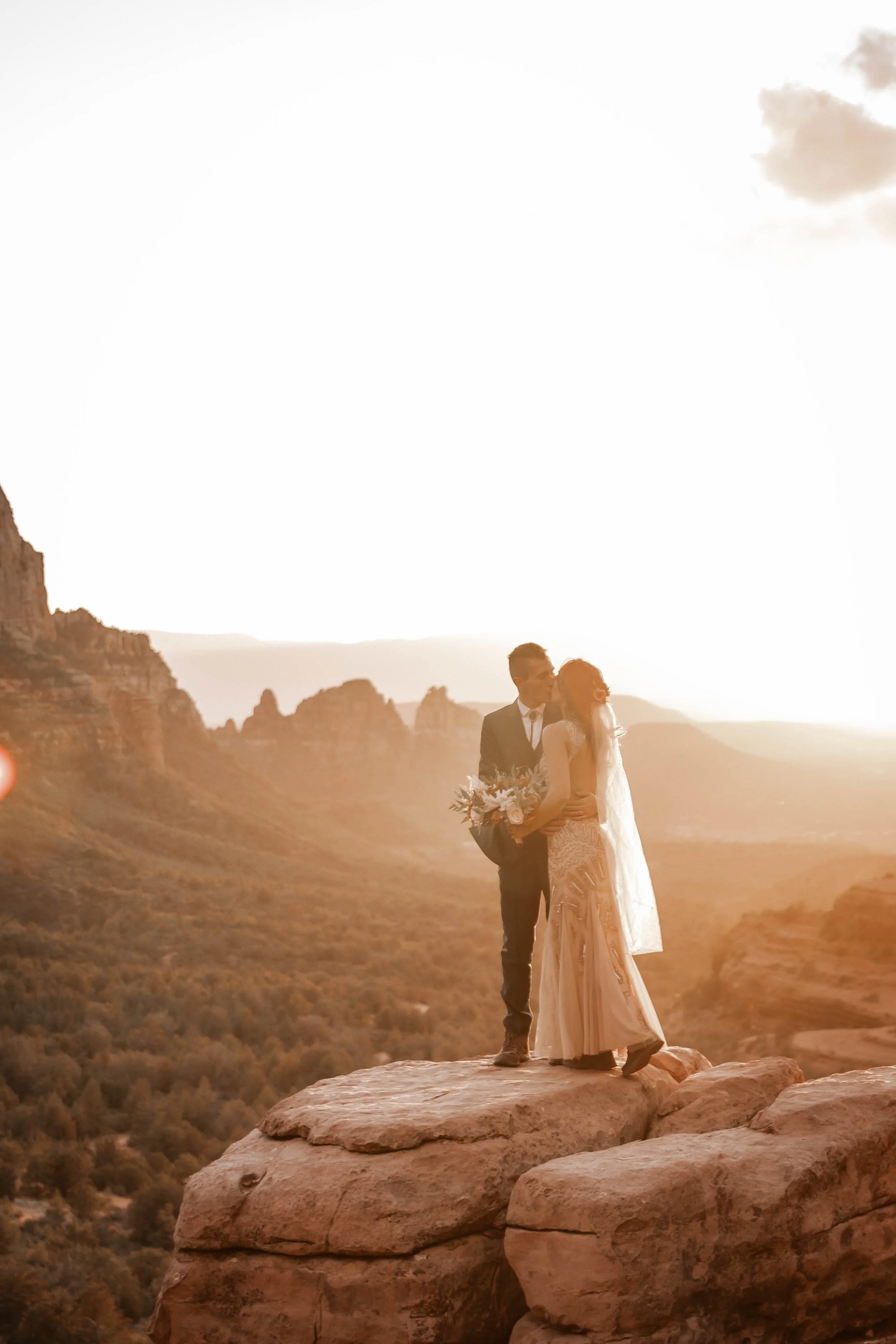 A bride and groom sharing a kiss during their wedding on a large rock formation at sunset with Bear Wallow valley and mountains in the background.