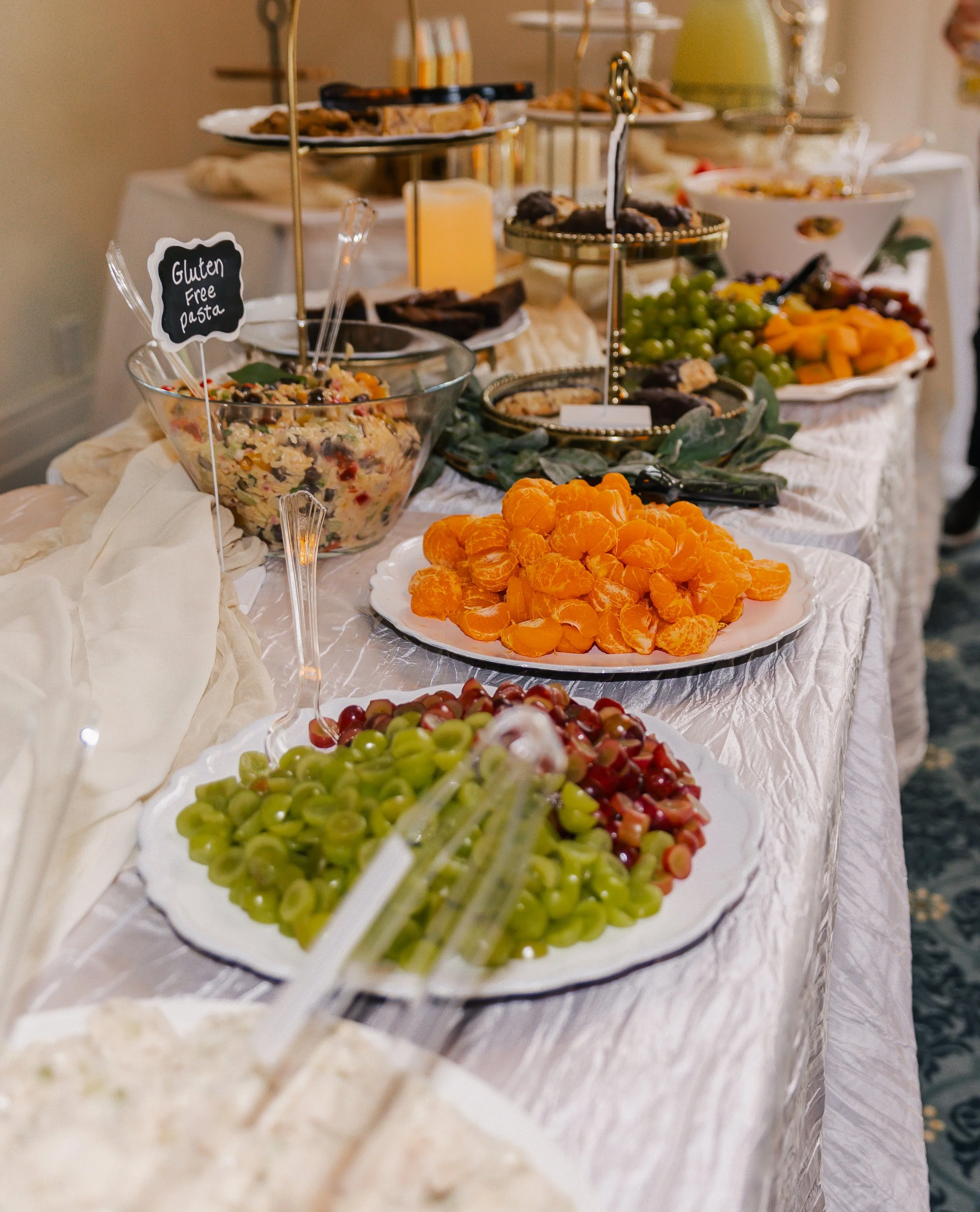 Fruit platter with grapes, mandarin oranges, and other fresh fruit on a buffet table with various dishes and desserts in the background.