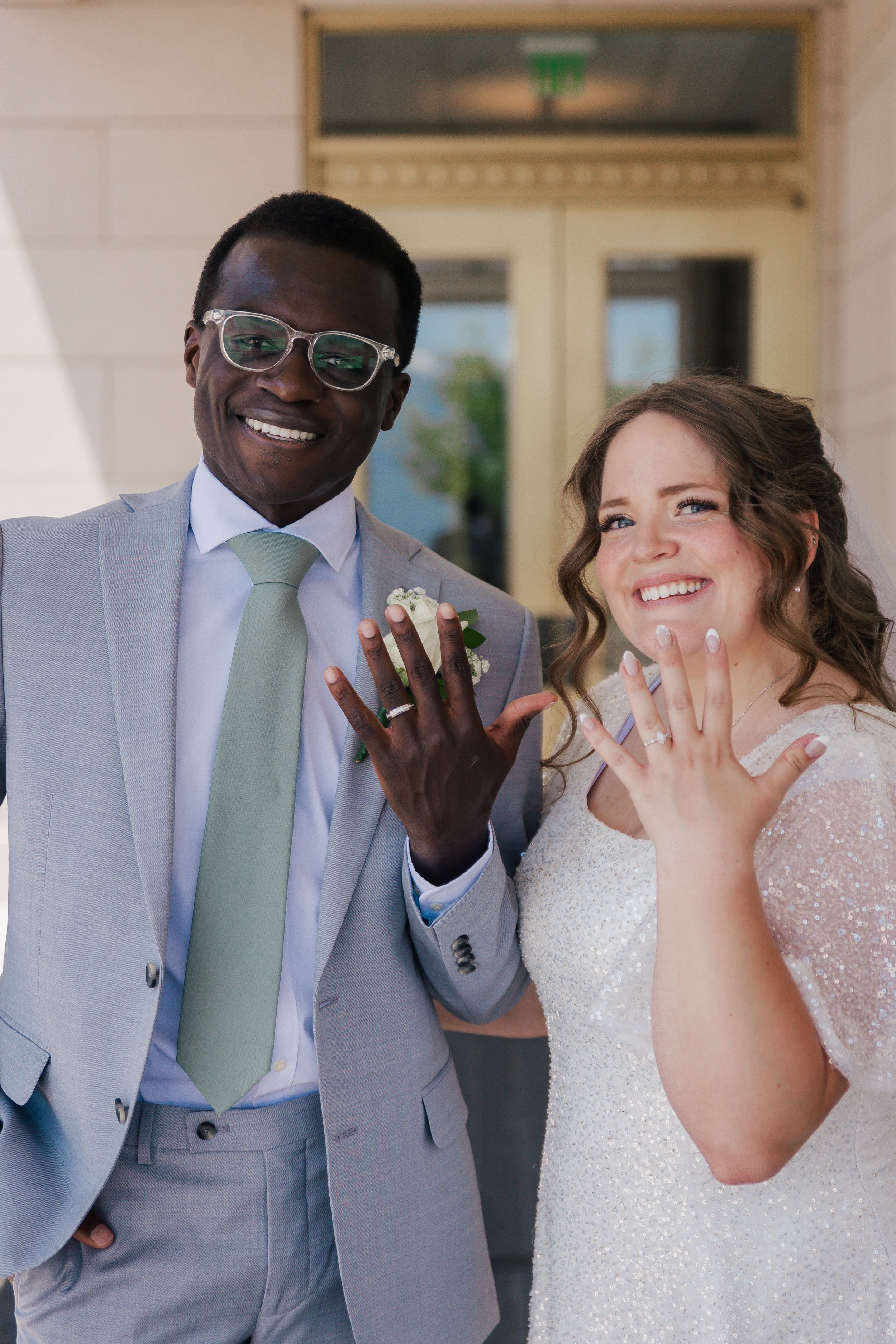 A happy couple displaying their wedding rings outside a building.