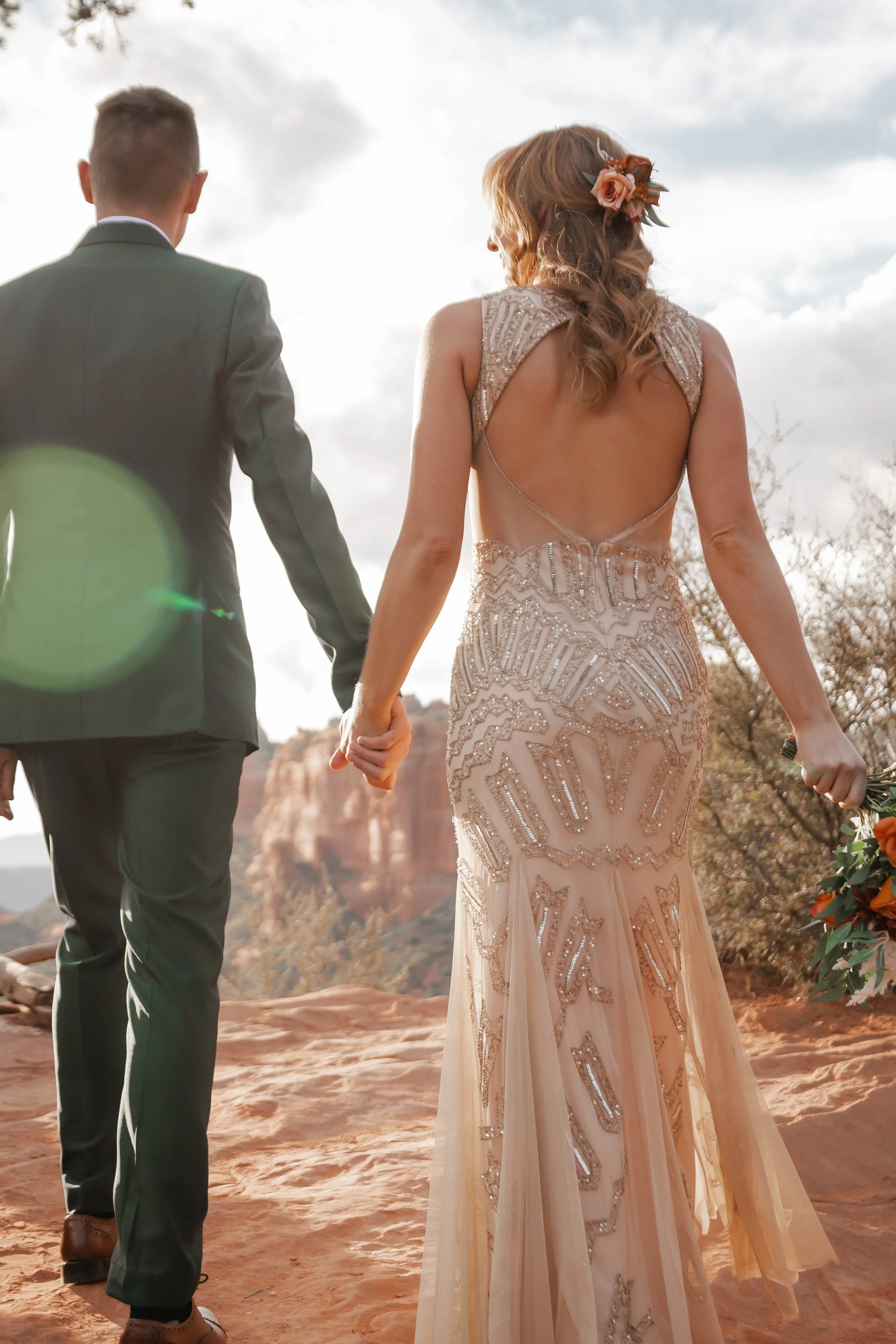 Couple in wedding attire holding hands outdoors with desert landscape and cliffs in background