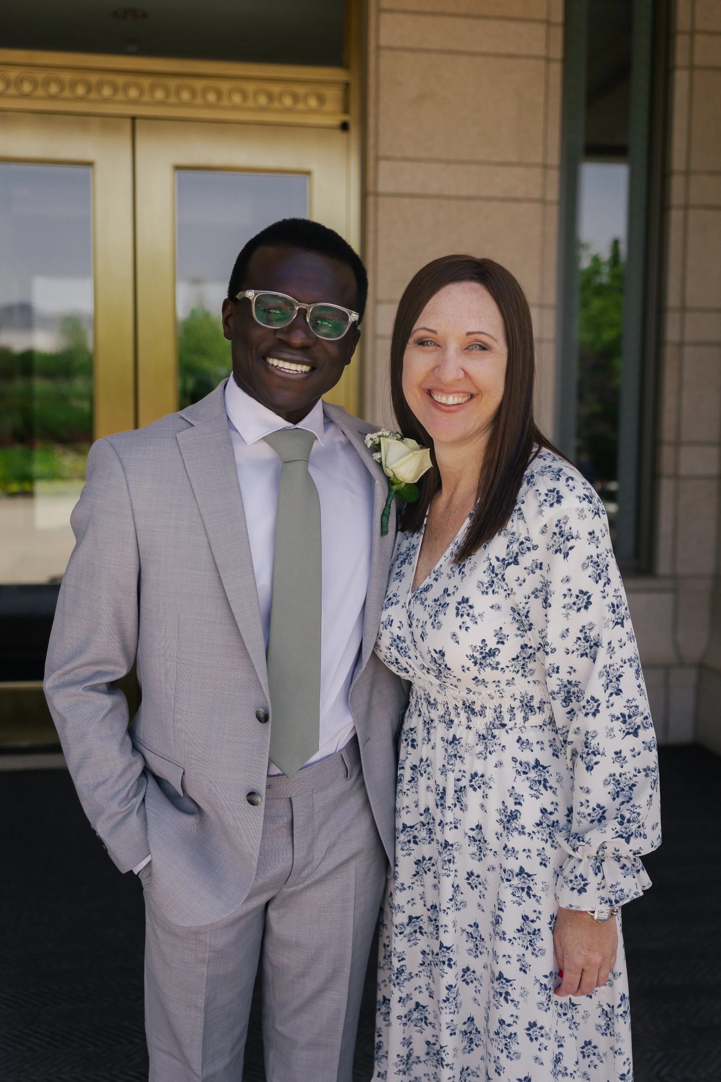 A couple dressed in formal attire smiling outside a building.