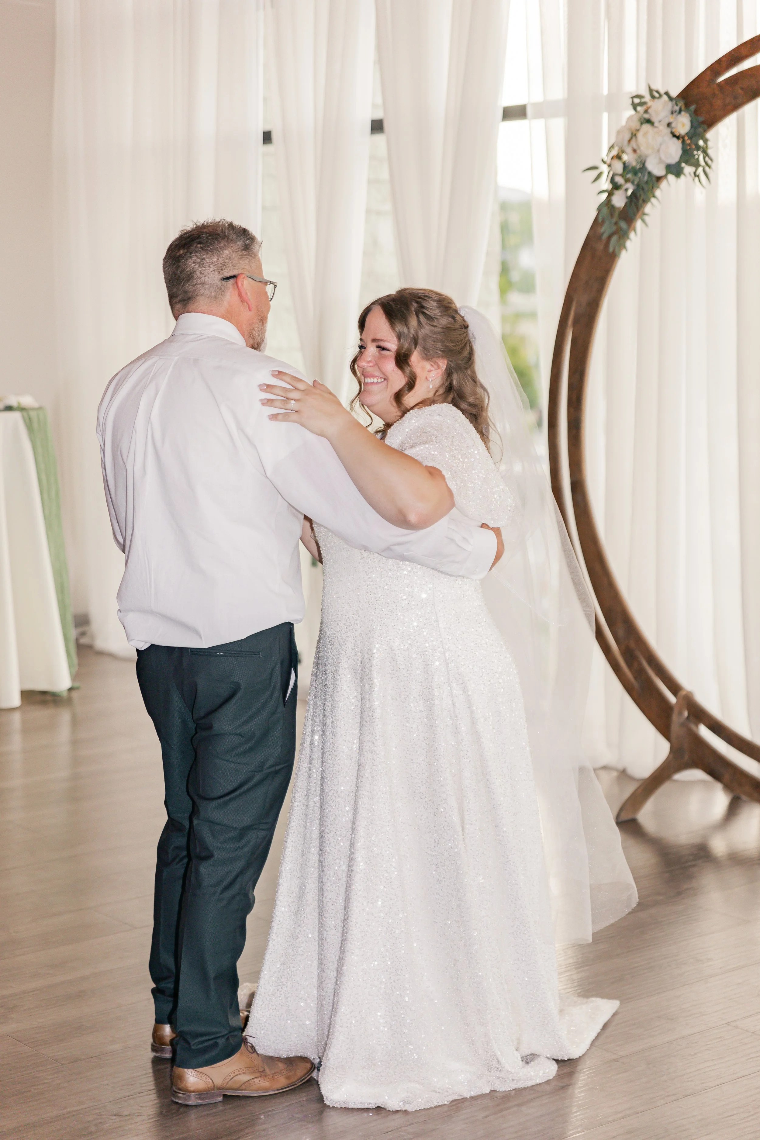 Bridal couple sharing a dance indoors at a wedding reception with artwork and curtains in the background.