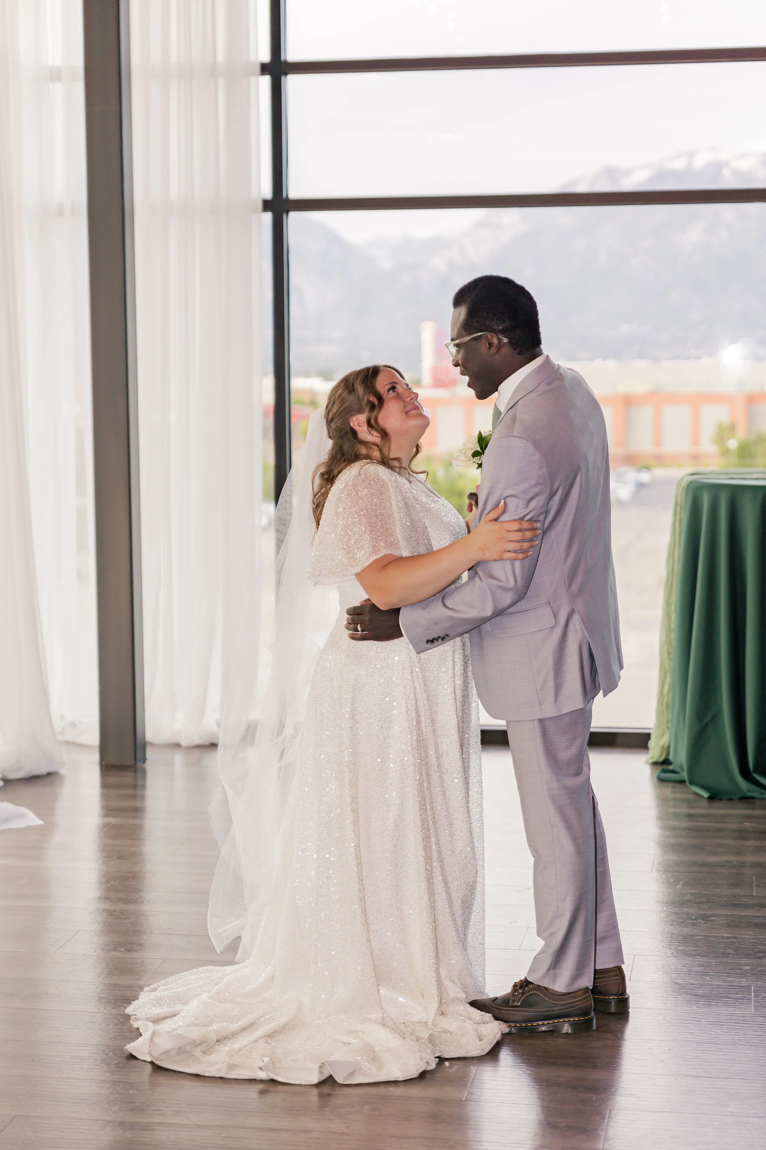 Bride and groom holding each other during their wedding ceremony indoors, with large windows and mountain view in the background.