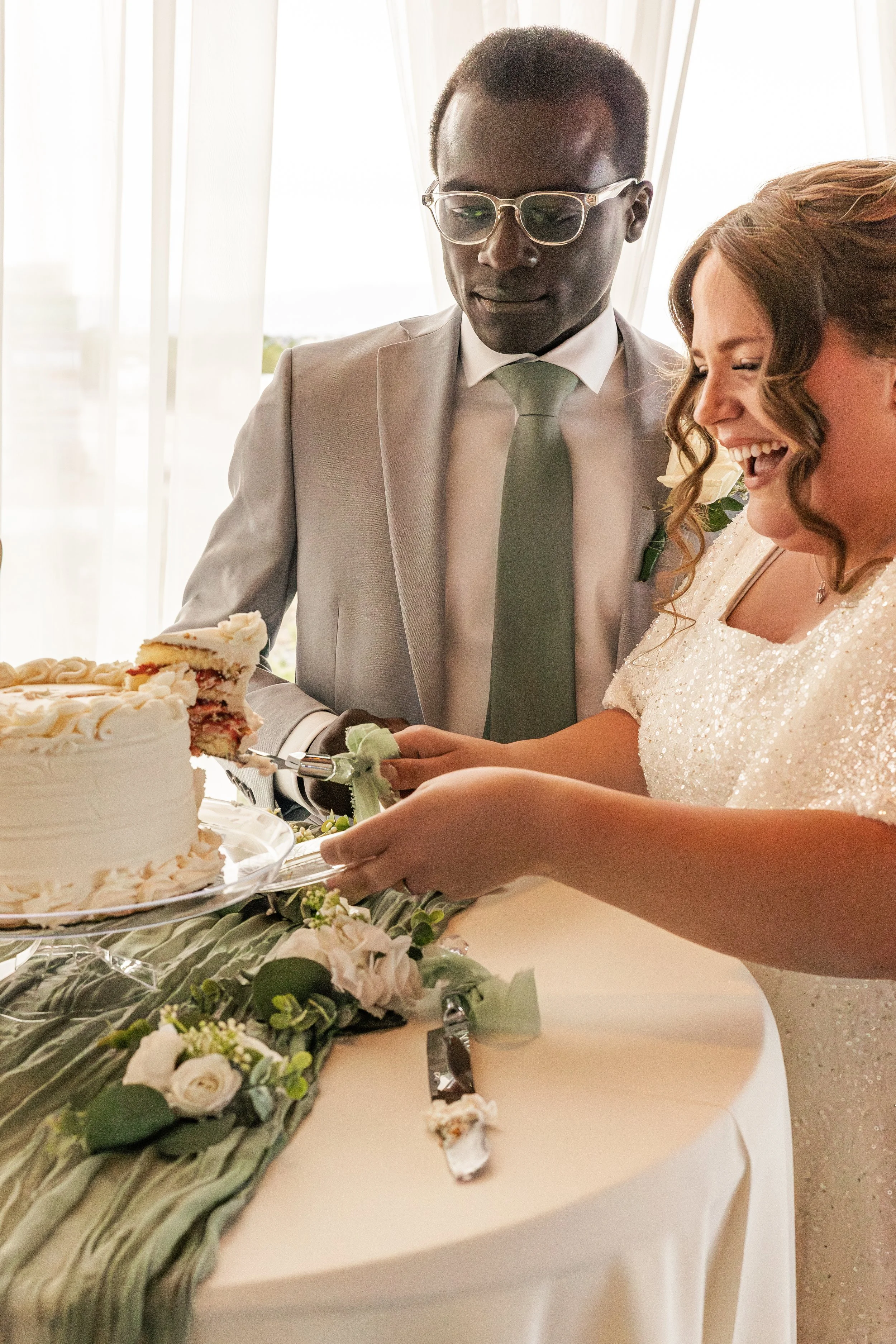 A bride and groom cutting a wedding cake together, smiling and happy, at their wedding reception.