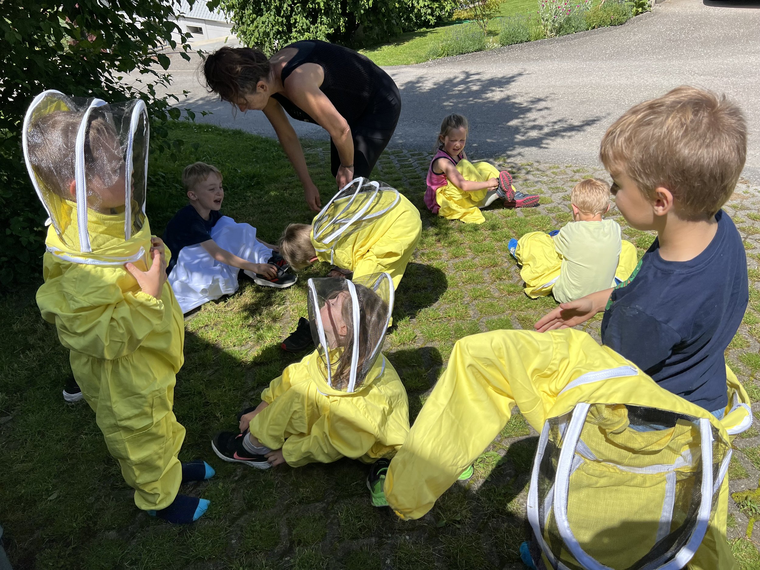 Die Schulkinder ziehen die Imkeranzüge an, dabei hilft die Lehrerin.