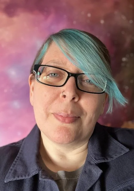 A headshot of Dr Char Goodwin who has blue hair and glasses