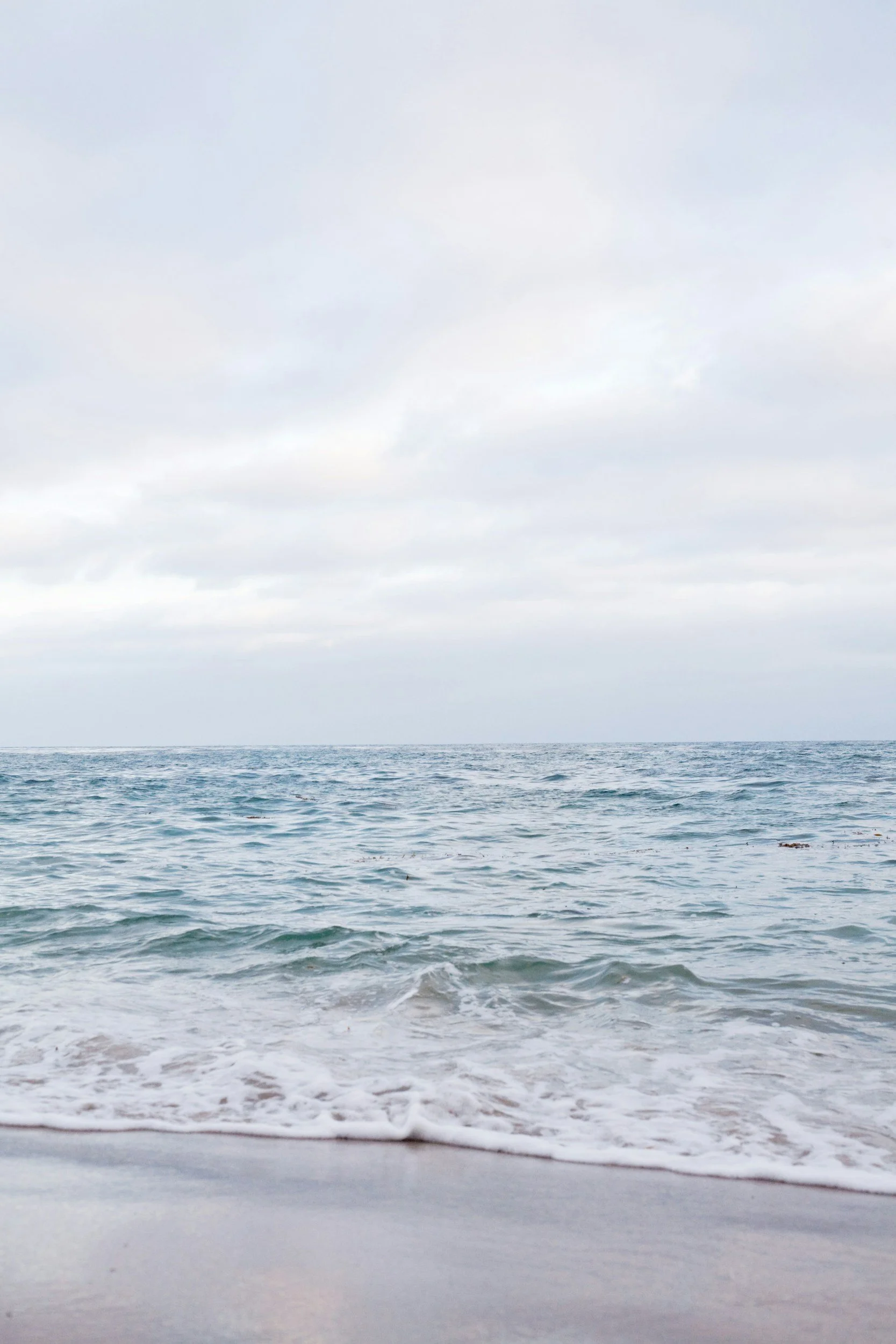 A calm ocean with gentle waves touching a sandy beach under a cloudy sky.
