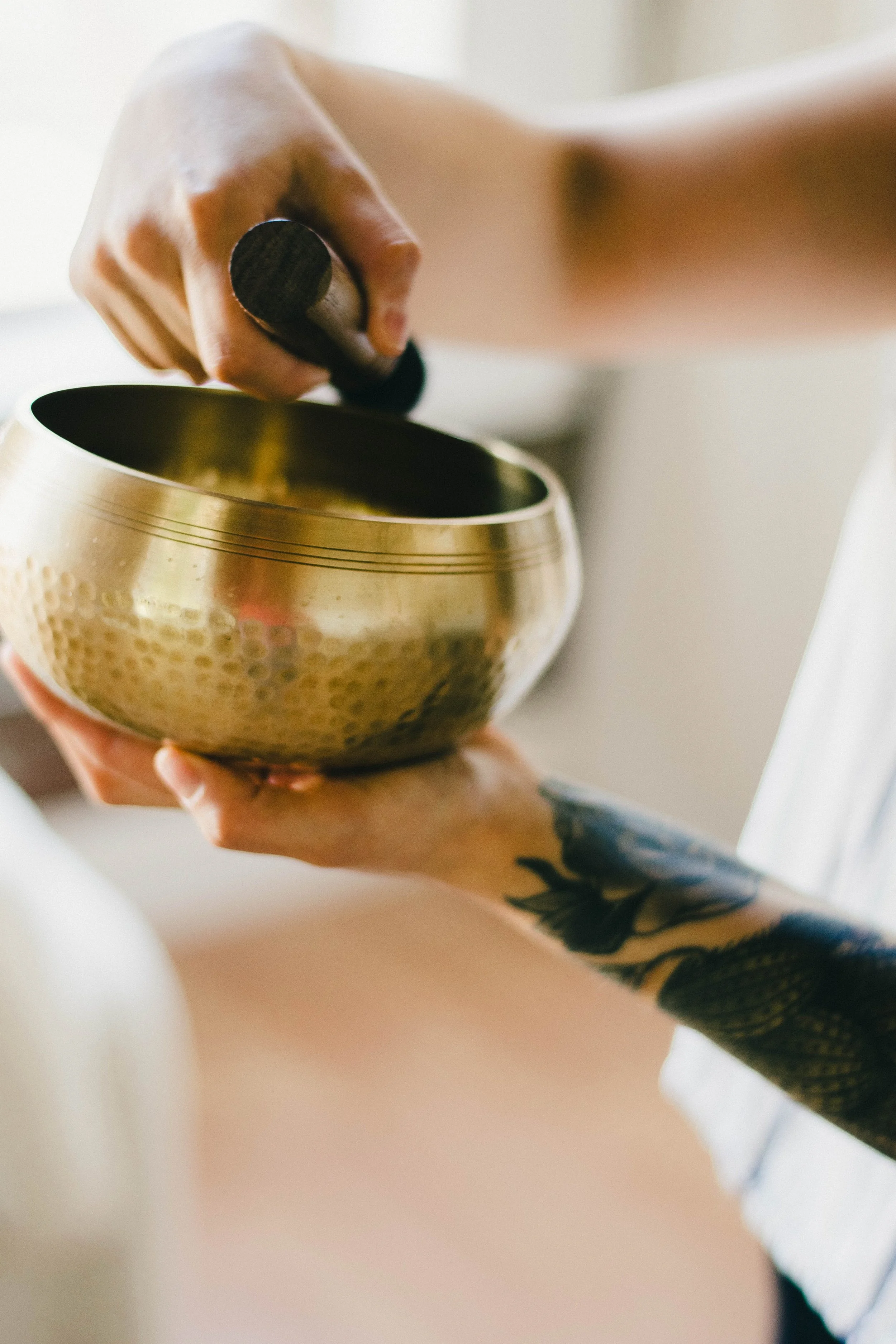 Person holding a singing bowl with one hand while using a mallet with the other hand.