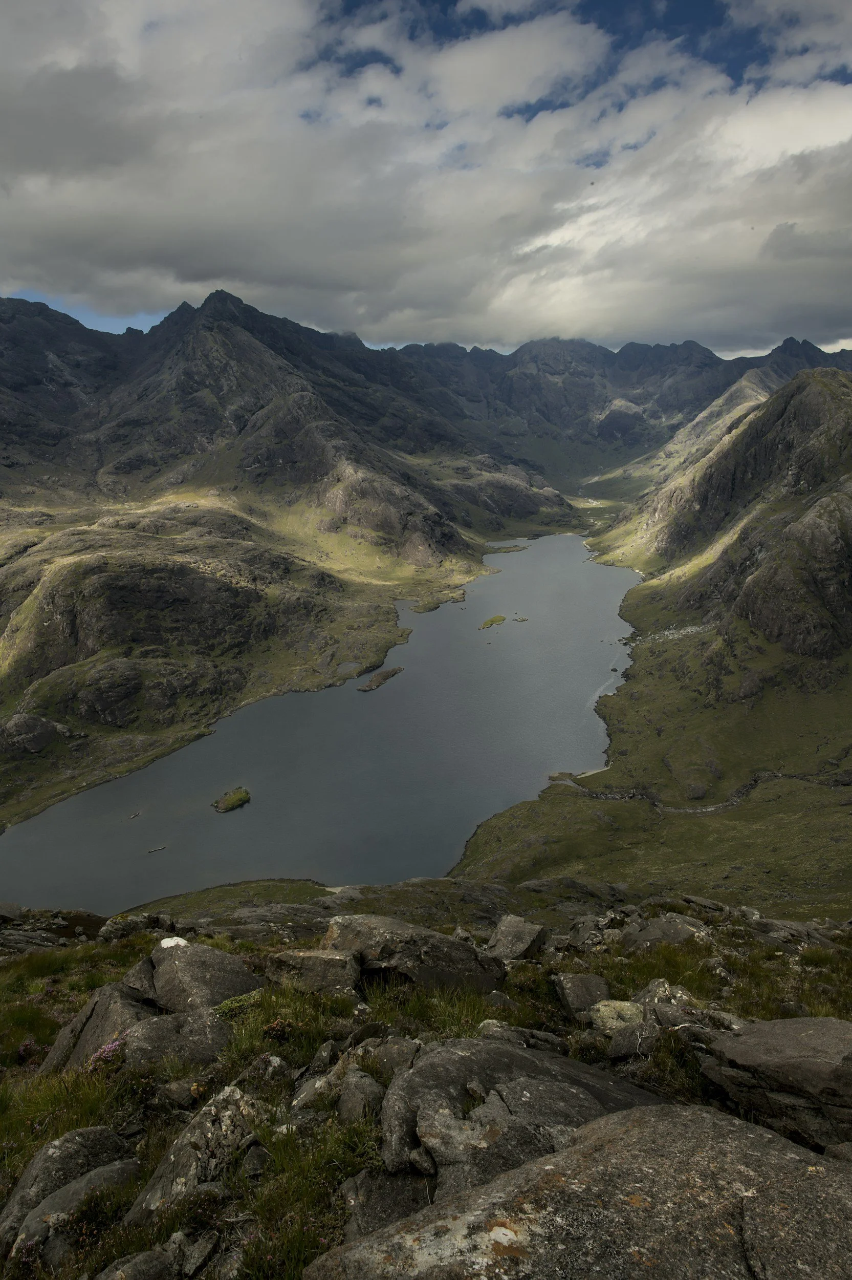 A mountainous landscape with a lake in the valley under a cloudy sky.