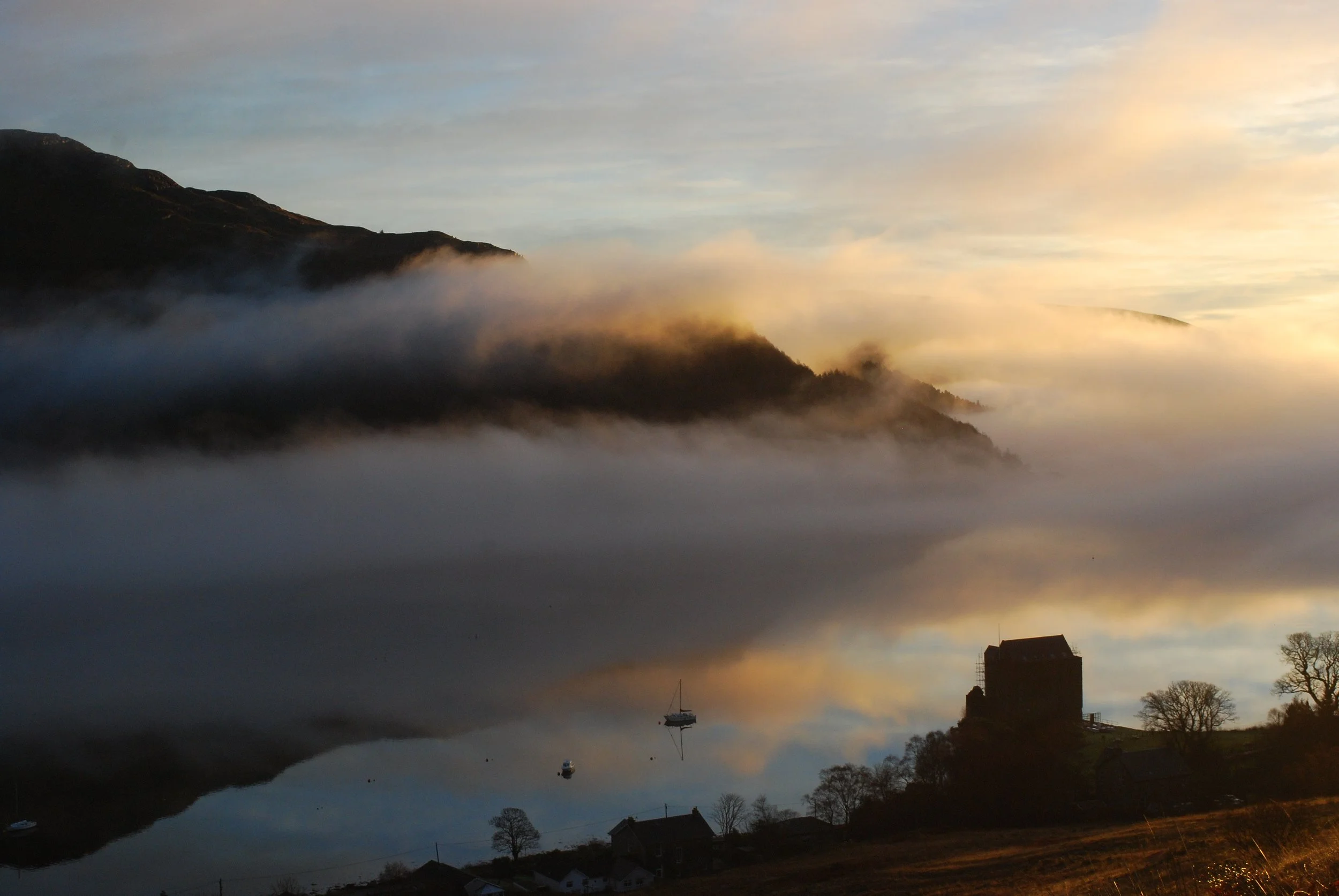 A rocky shoreline by the ocean with a hill in the background and a cloudy sky.