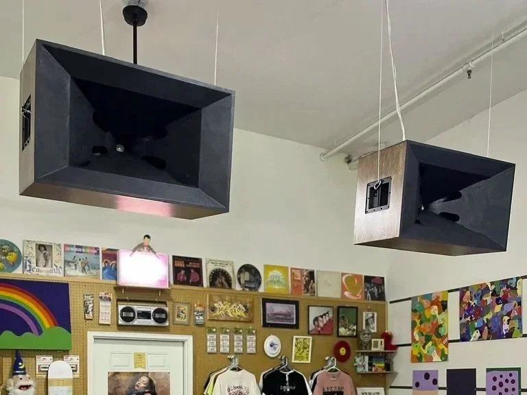 Indoor room with attached speaker speakers hanging from ceiling, colorful wall art, record albums, and photos on a pegboard wall.